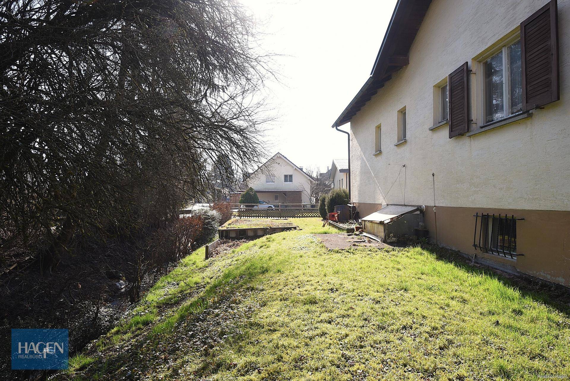 Sonniger Gartenbereich neben dem Haus mit Rasenfläche und Blick auf die umliegende Bebauung.