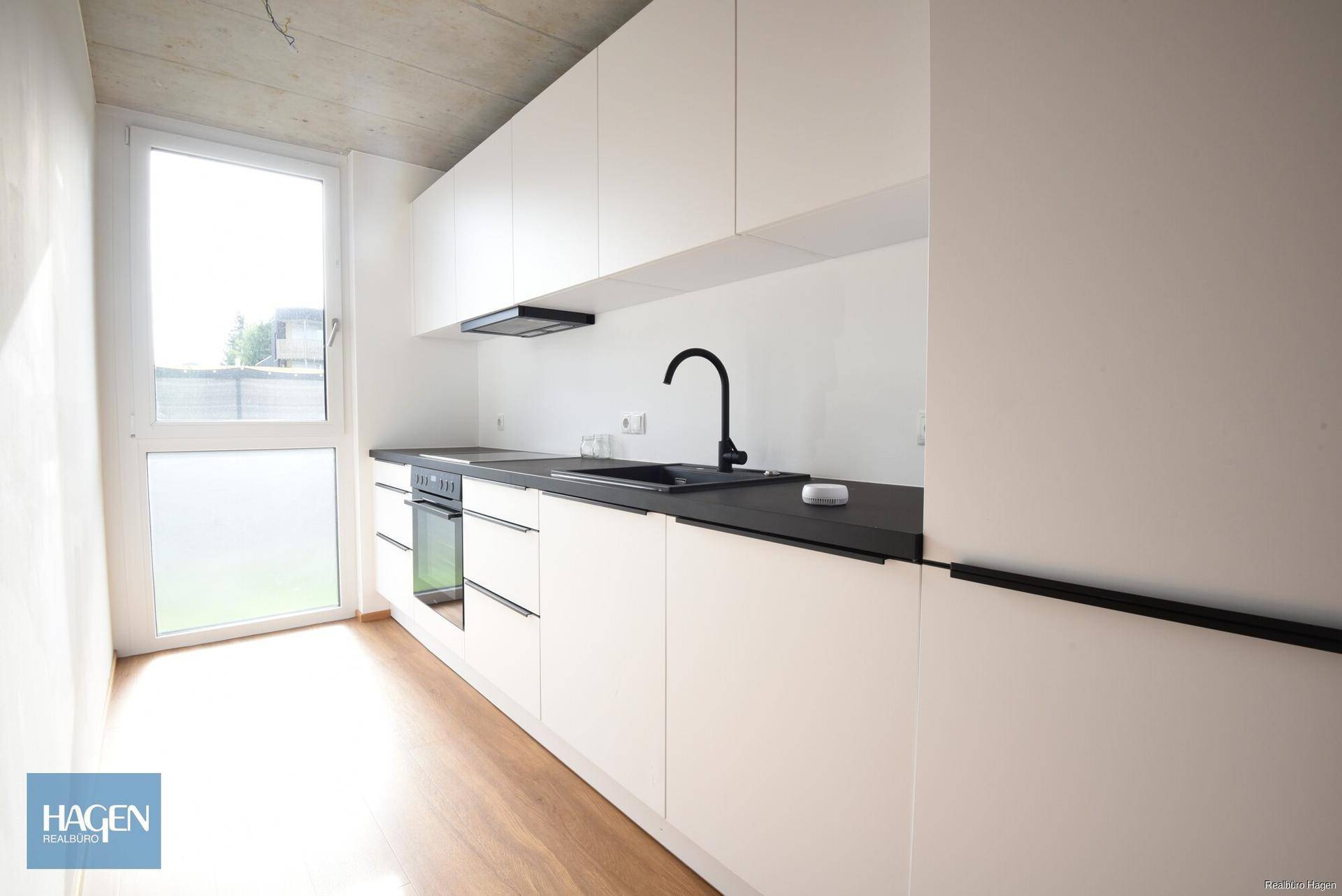 Moderne Küche mit weißen Schränken, schwarzer Arbeitsplatte und integriertem Backofen.