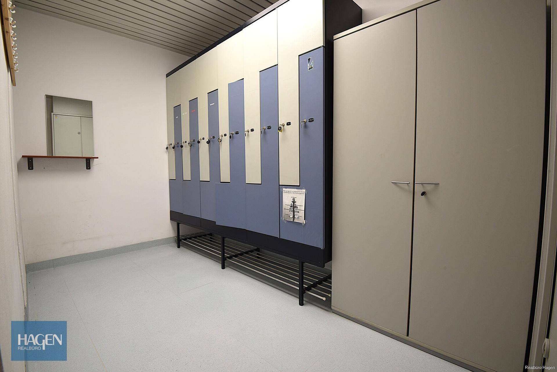 Umkleideraum mit blauen und grauen Spinden sowie einem kleinen Spiegel an der Wand.