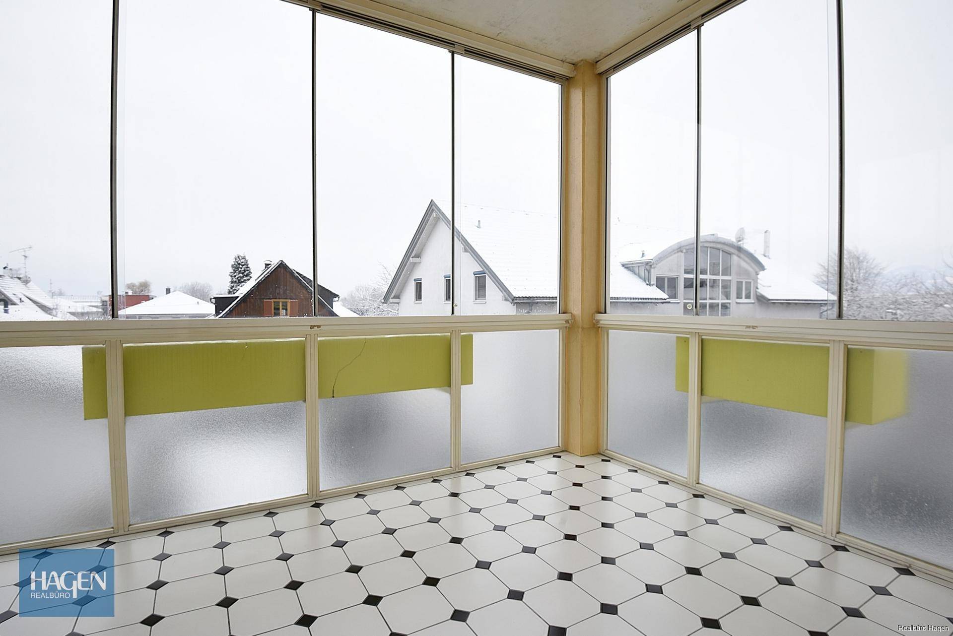 Verglaster Wintergarten mit Fliesenboden und Blick auf die verschneite Umgebung.