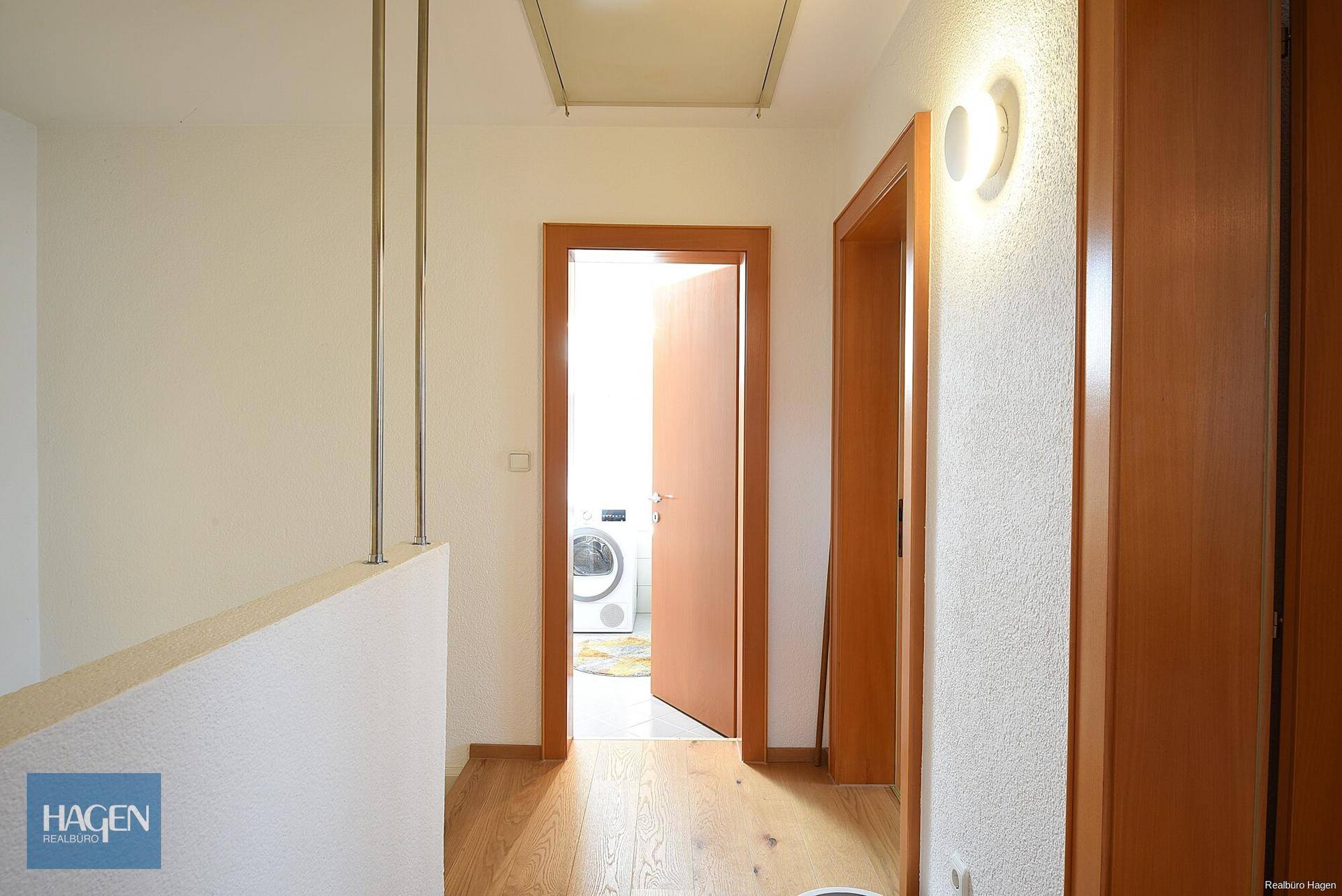 Oberer Flur mit Holzboden und Zugang zu weiteren Räumen, inklusive Waschküche mit Waschmaschine.