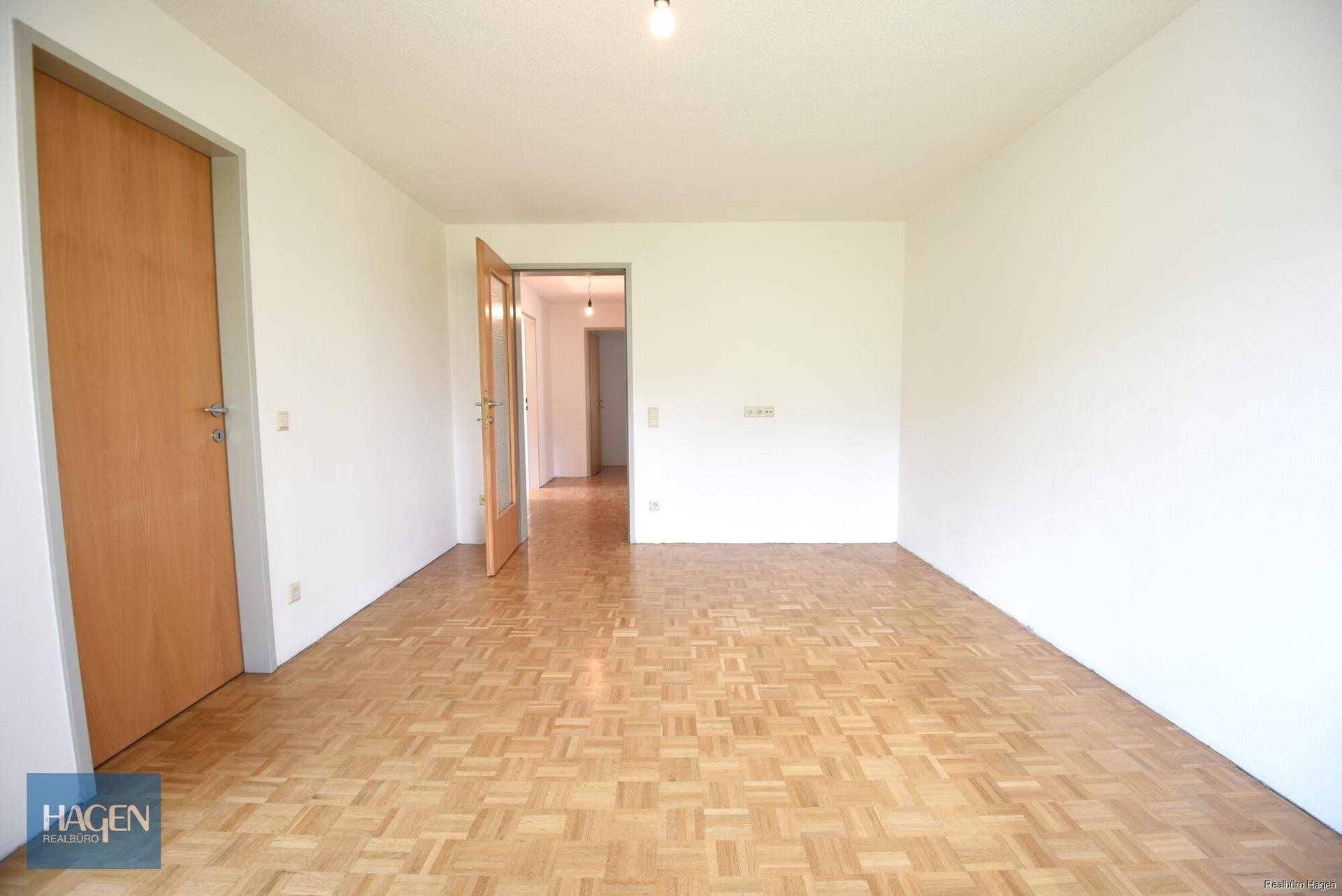 Geräumiger, heller Raum mit Parkettboden und Holztüren, Blick in den Flur.