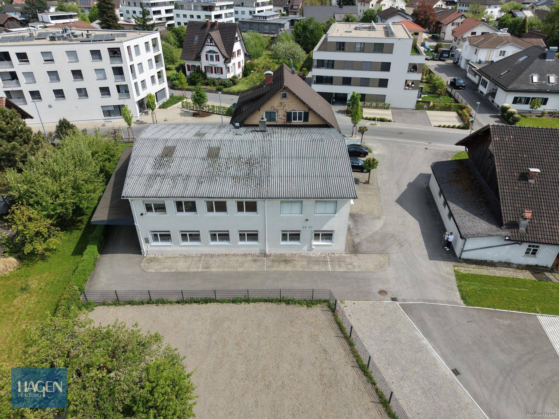 Luftaufnahme eines weißen Gebäudes mit Flachdach und umliegenden Parkflächen in einer städtischen Umgebung.