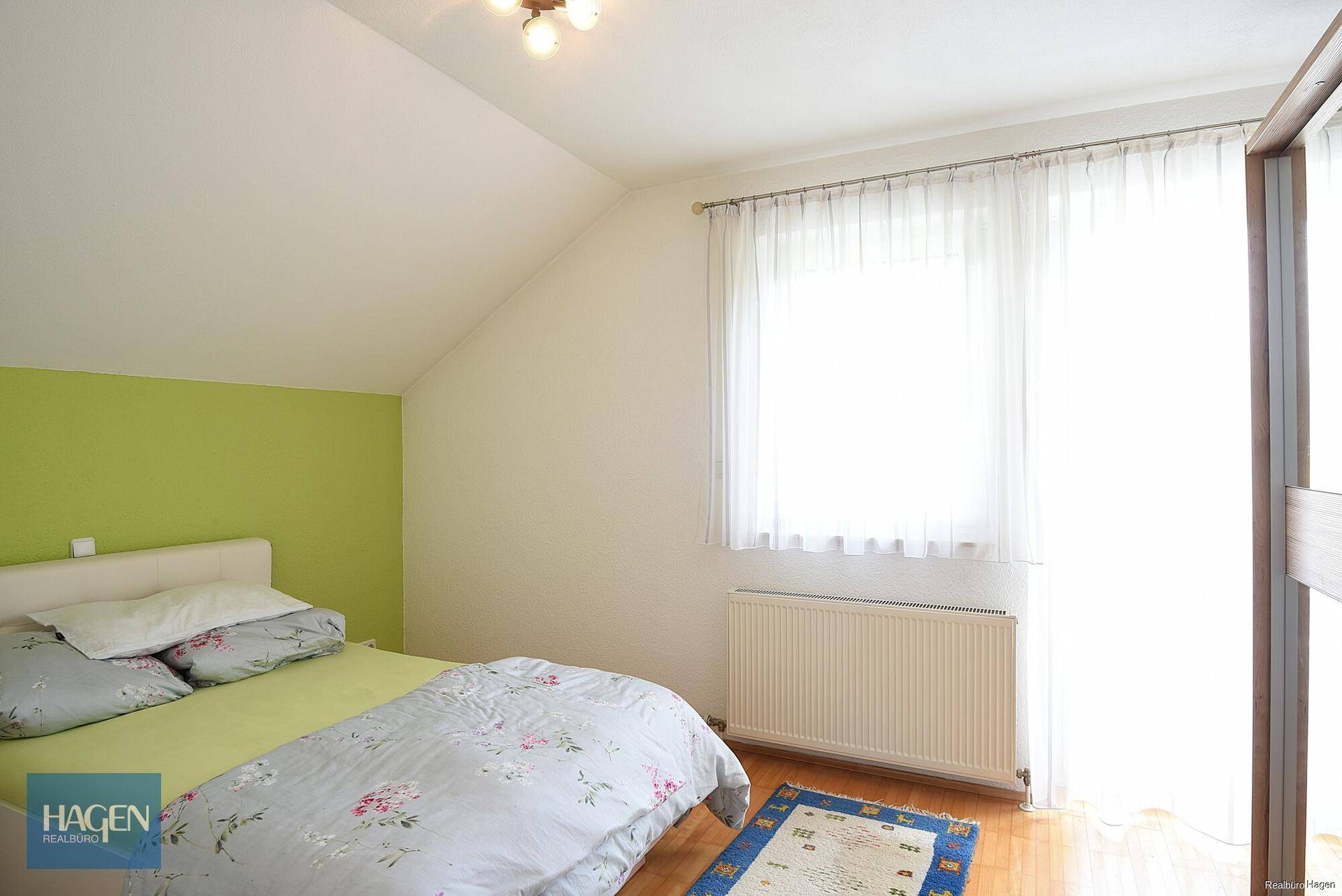 Schlafzimmer mit Dachschräge, Holzboden, farbiger Akzentwand und viel natürlichem Licht.