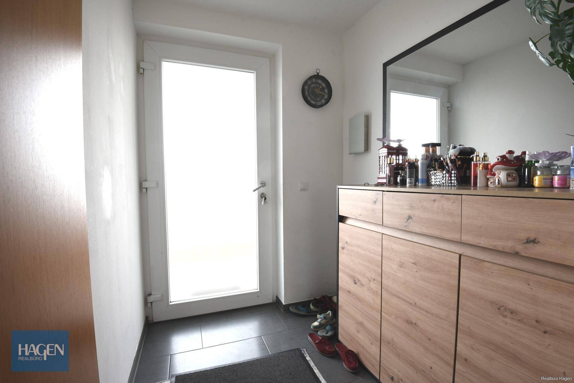 Heller Eingangsbereich mit dunklen Fliesen, Schuhschrank und großem Wandspiegel.