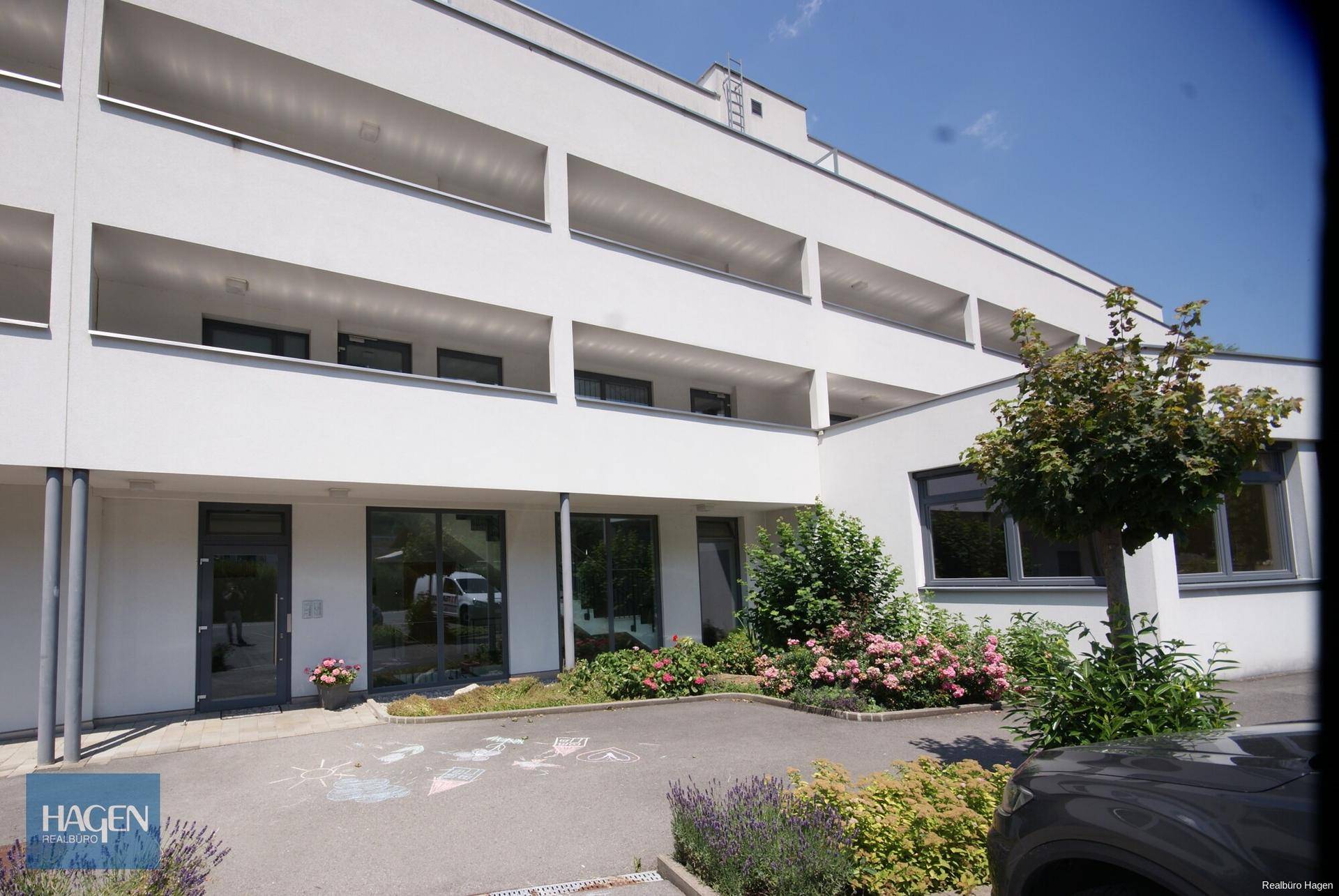 Moderne Wohnanlage mit weißer Fassade, Balkonen und gepflegter Außenanlage.