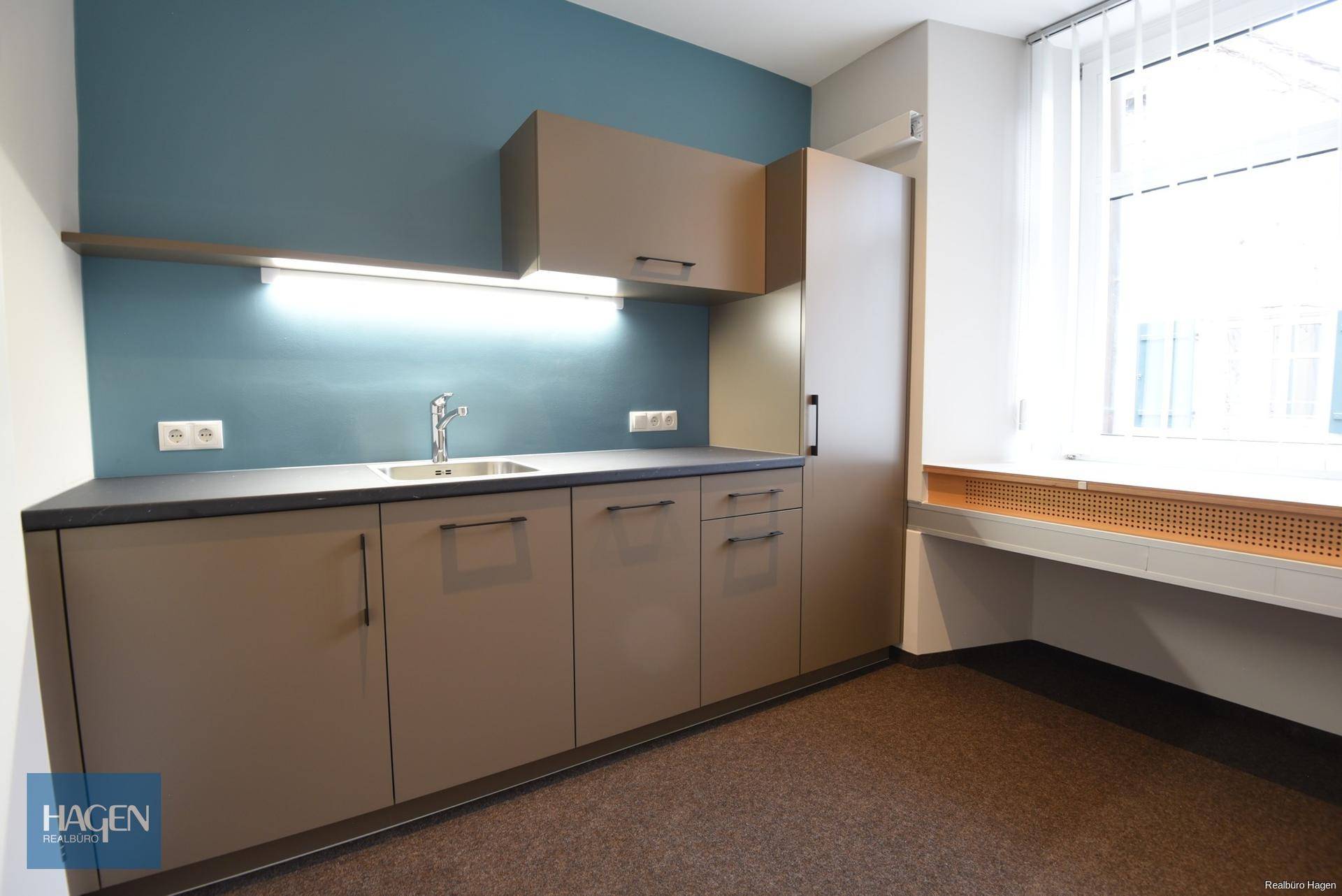 Moderne Teeküche mit braunen Schränken, Spüle und blauer Akzentwand in einem Büro.