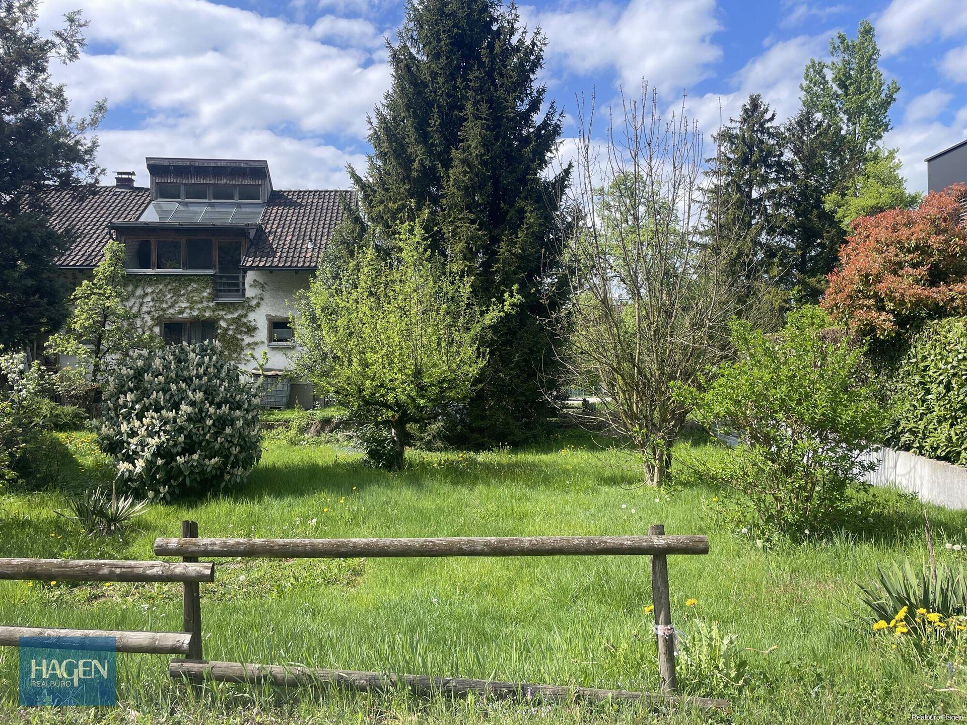 Weitläufiger Gartenbereich mit Rasenfläche und verschiedenen Bäumen unter sonnigem Himmel.