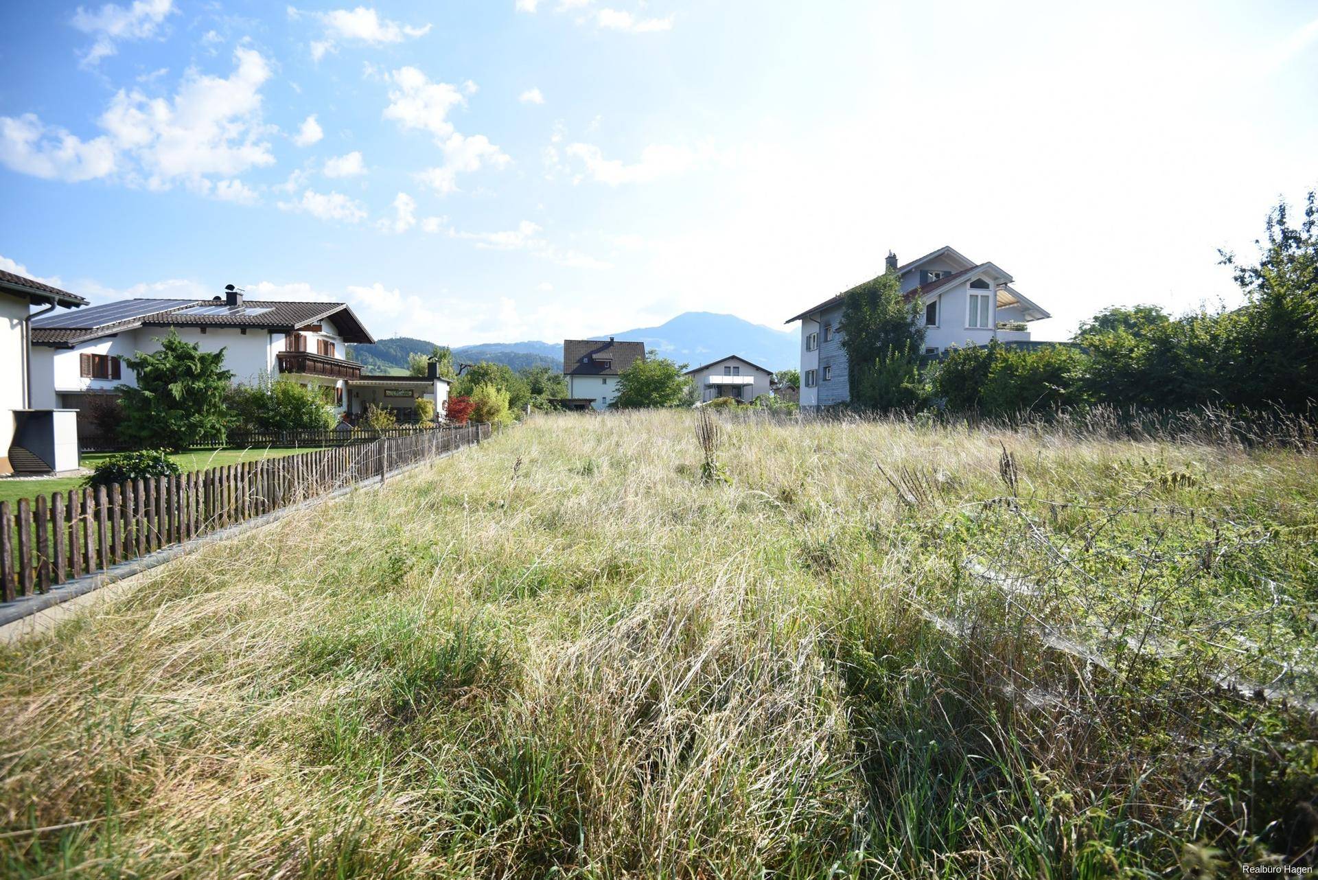 Offenes Grundstück mit hohem Gras, umgeben von Wohnhäusern und mit Bergsicht.