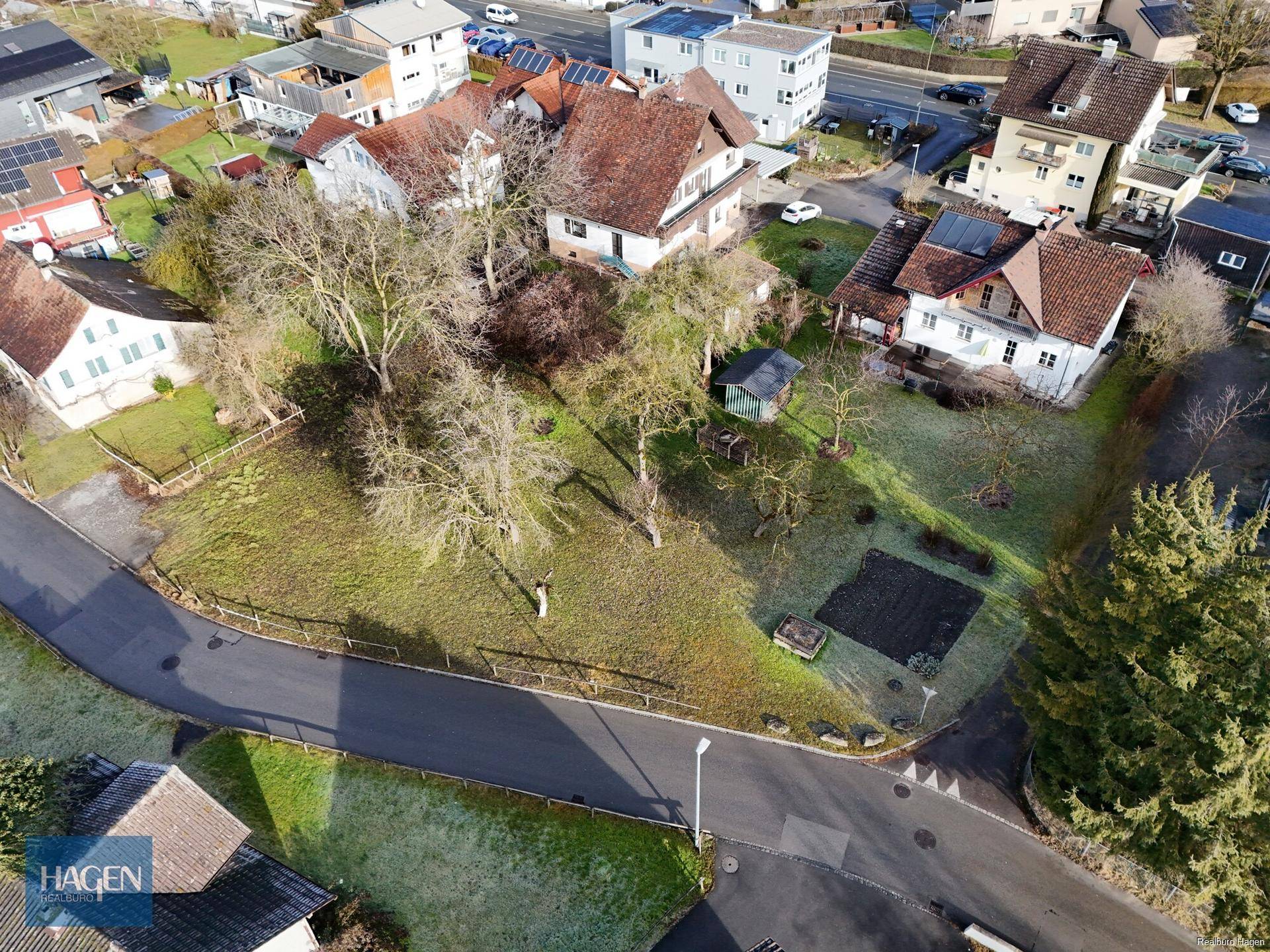 Luftaufnahme eines Grundstücks mit umgebenden Wohnhäusern und Straßen in einer sonnigen Landschaft.