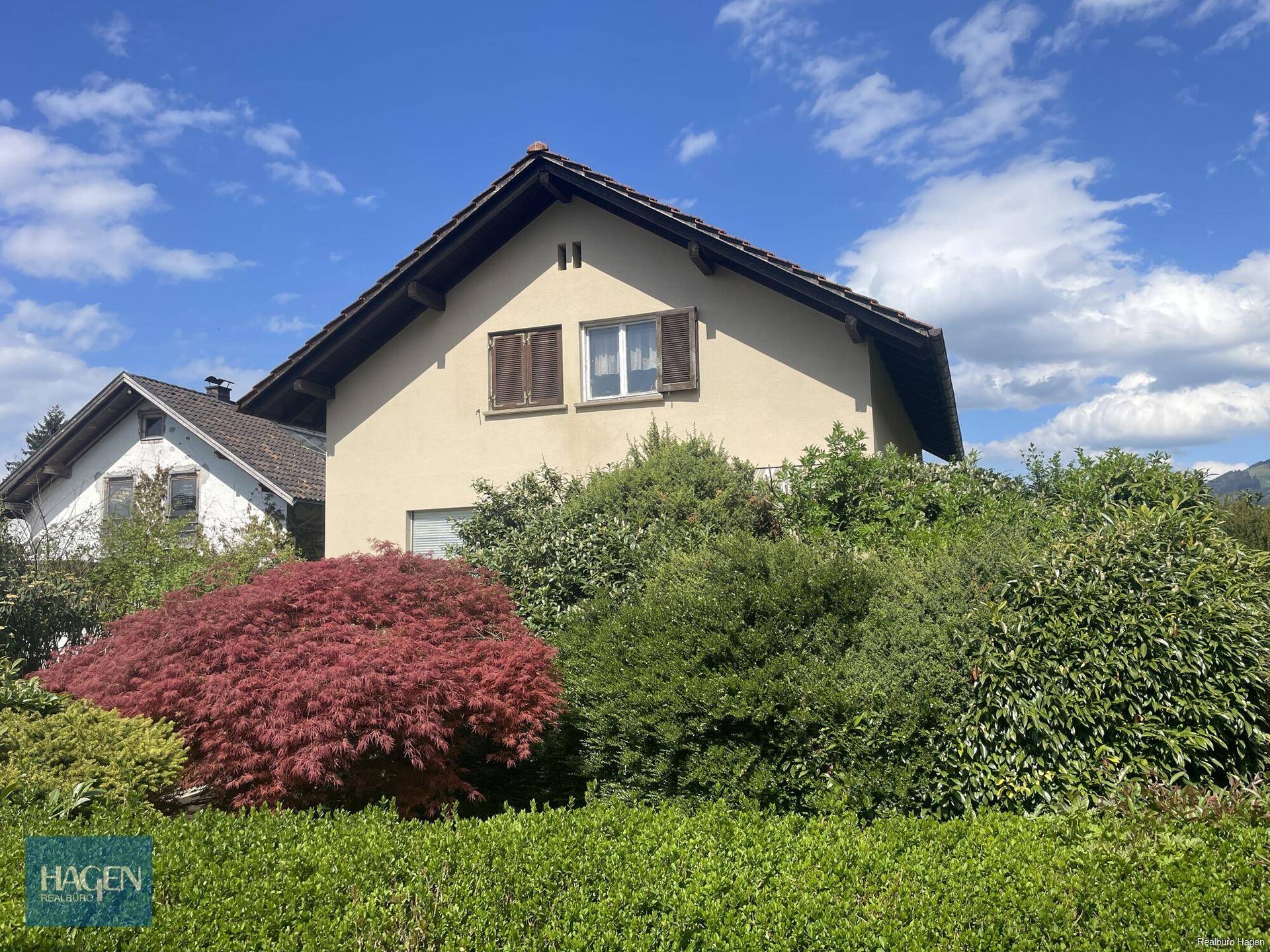 Das Haus von außen mit traditionellem Satteldach, umgeben von grünen Sträuchern und Bäumen.