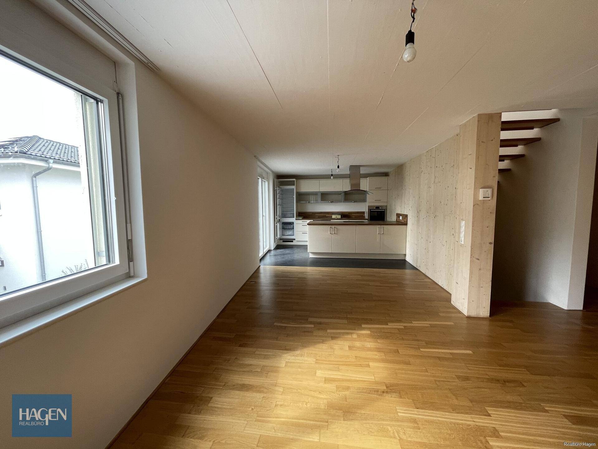 Offener Wohnbereich mit Holzboden und integrierter Küche, hell durch große Fenster.
