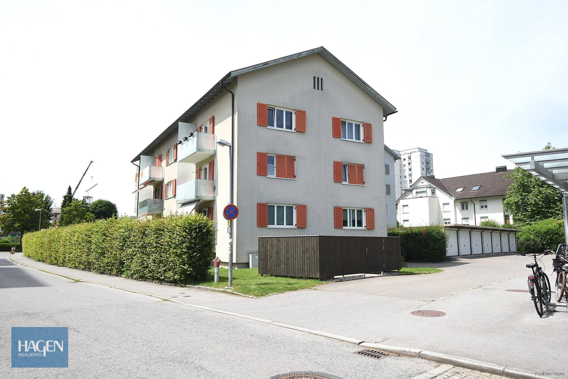 Ansicht eines Mehrfamilienhauses mit Balkonen und grüner Hecke an der Straßenseite, gut gepflegt.