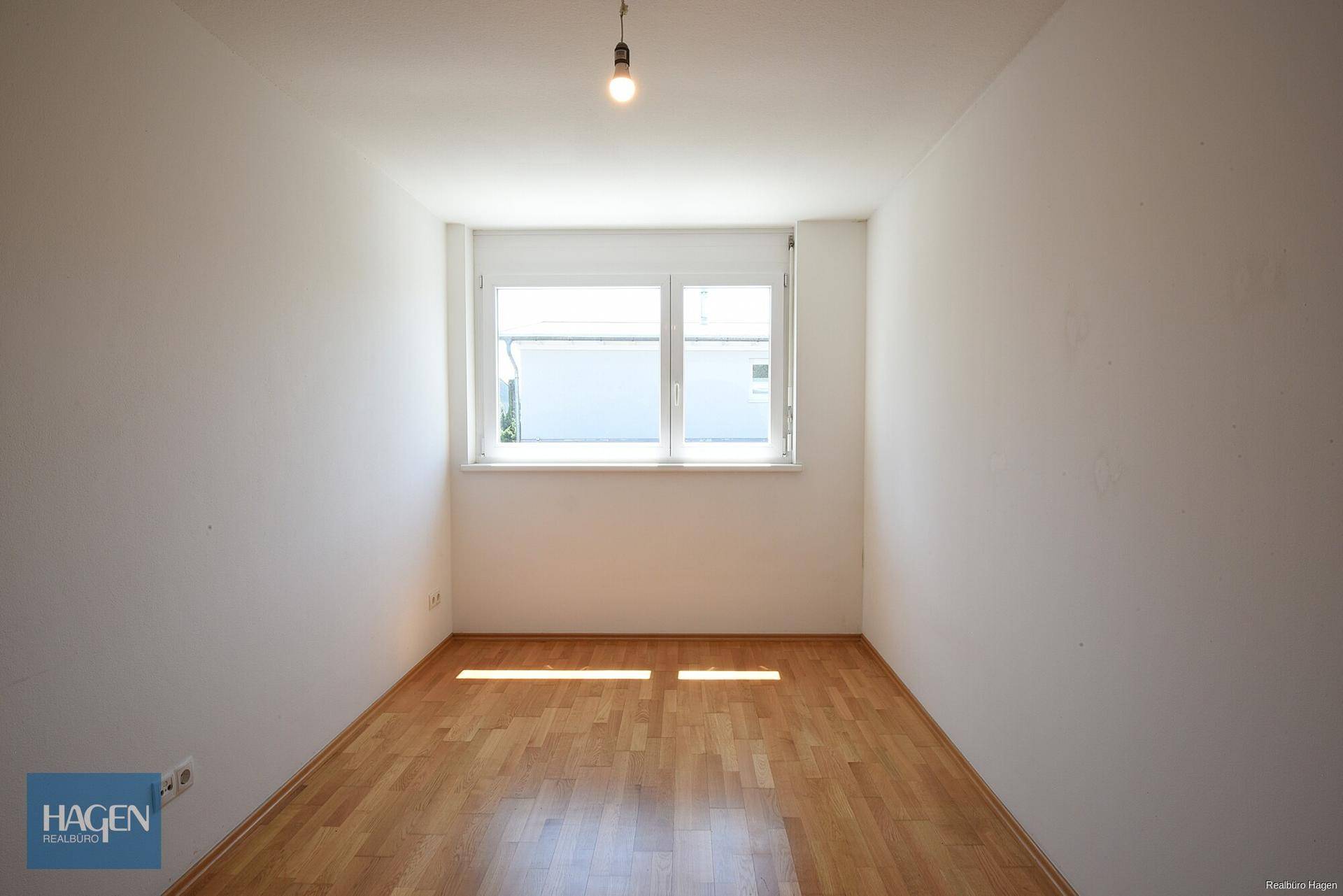 Geräumiges Zimmer mit hellem Holzboden und einem großen Fenster, das für gute Belichtung sorgt.