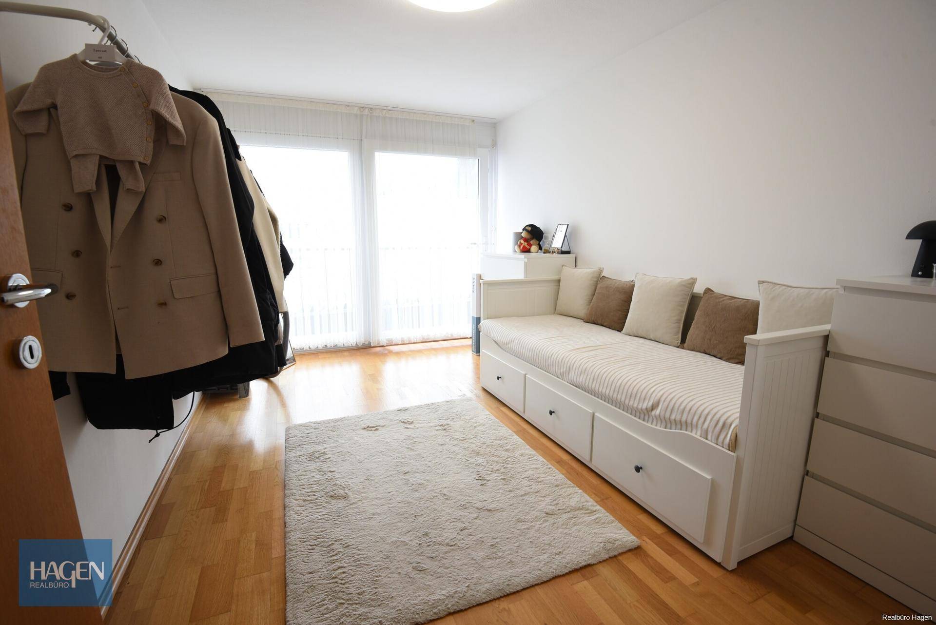 Helles Zimmer mit Tagesbett, Parkettboden und Zugang zu einem französischen Balkon.
