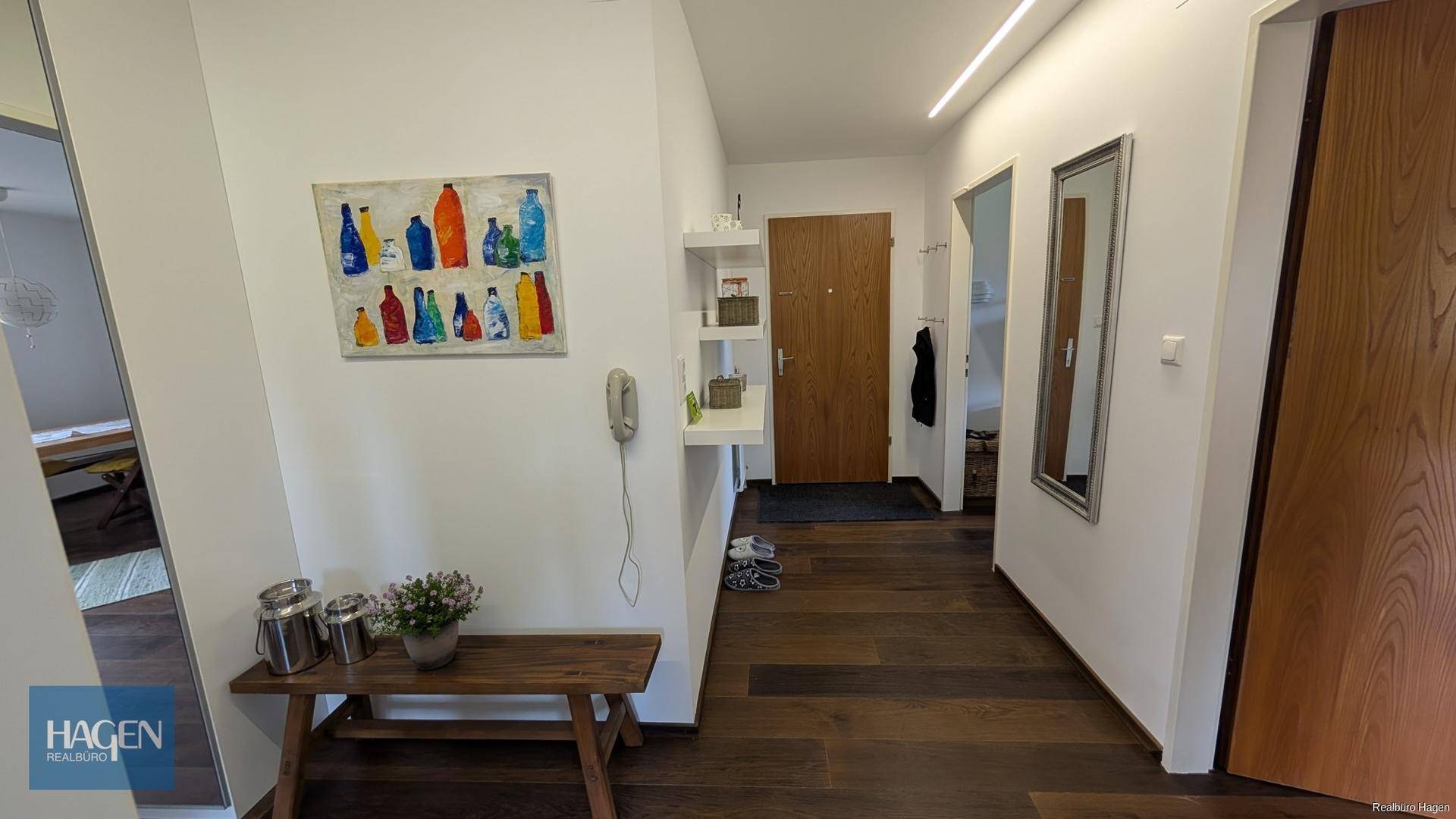 Heller Eingangsbereich mit dunklem Holzboden, weiß gestrichenen Wänden und einem großen Spiegel.