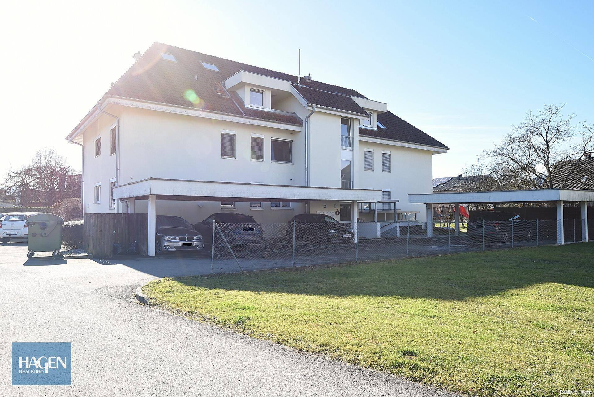 Rückansicht des Gebäudes mit überdachten Carports und einer gepflegten Rasenfläche.