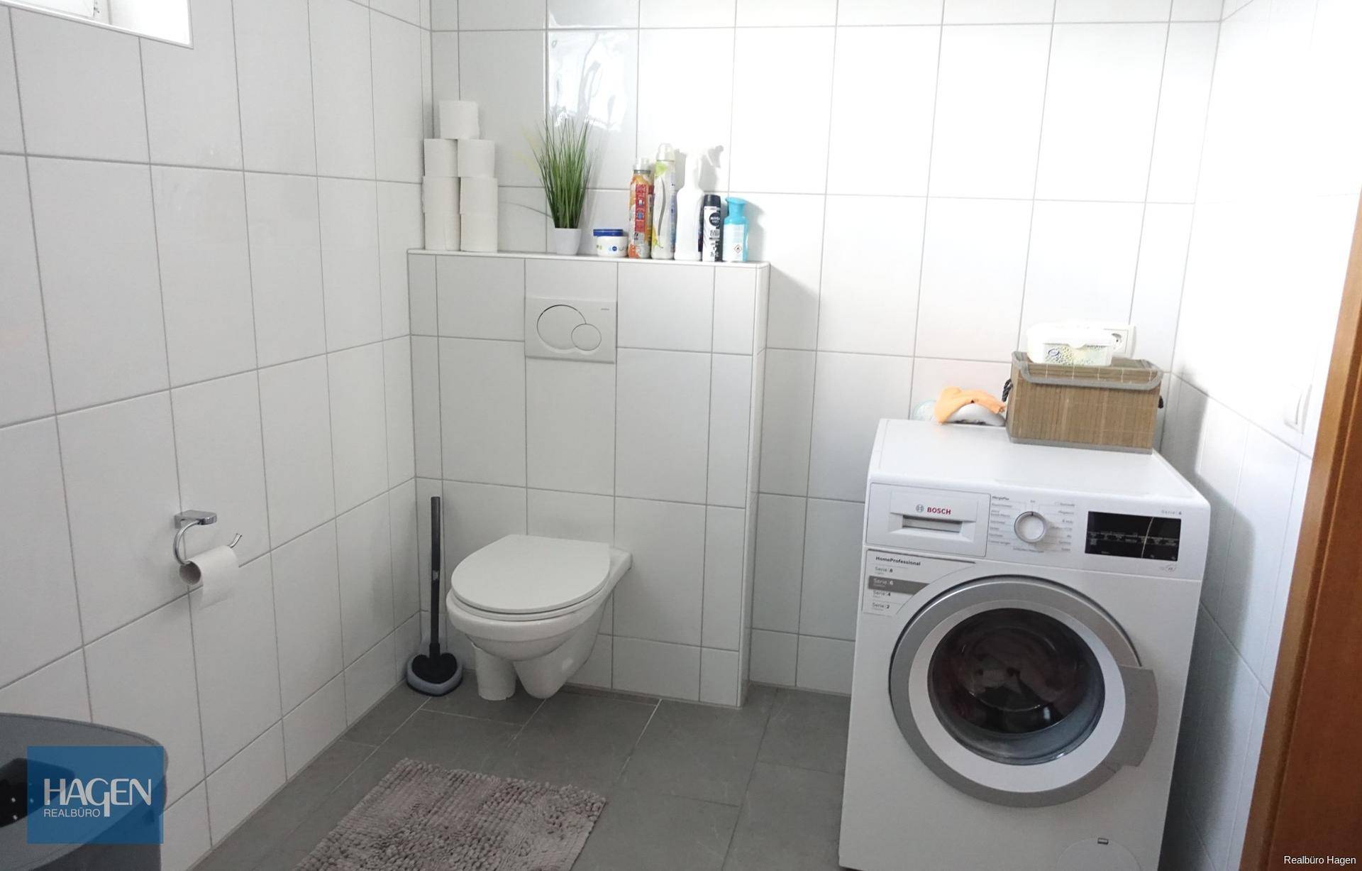 Modern gefliestes WC mit wandhängender Toilette und integrierter Waschmaschine.