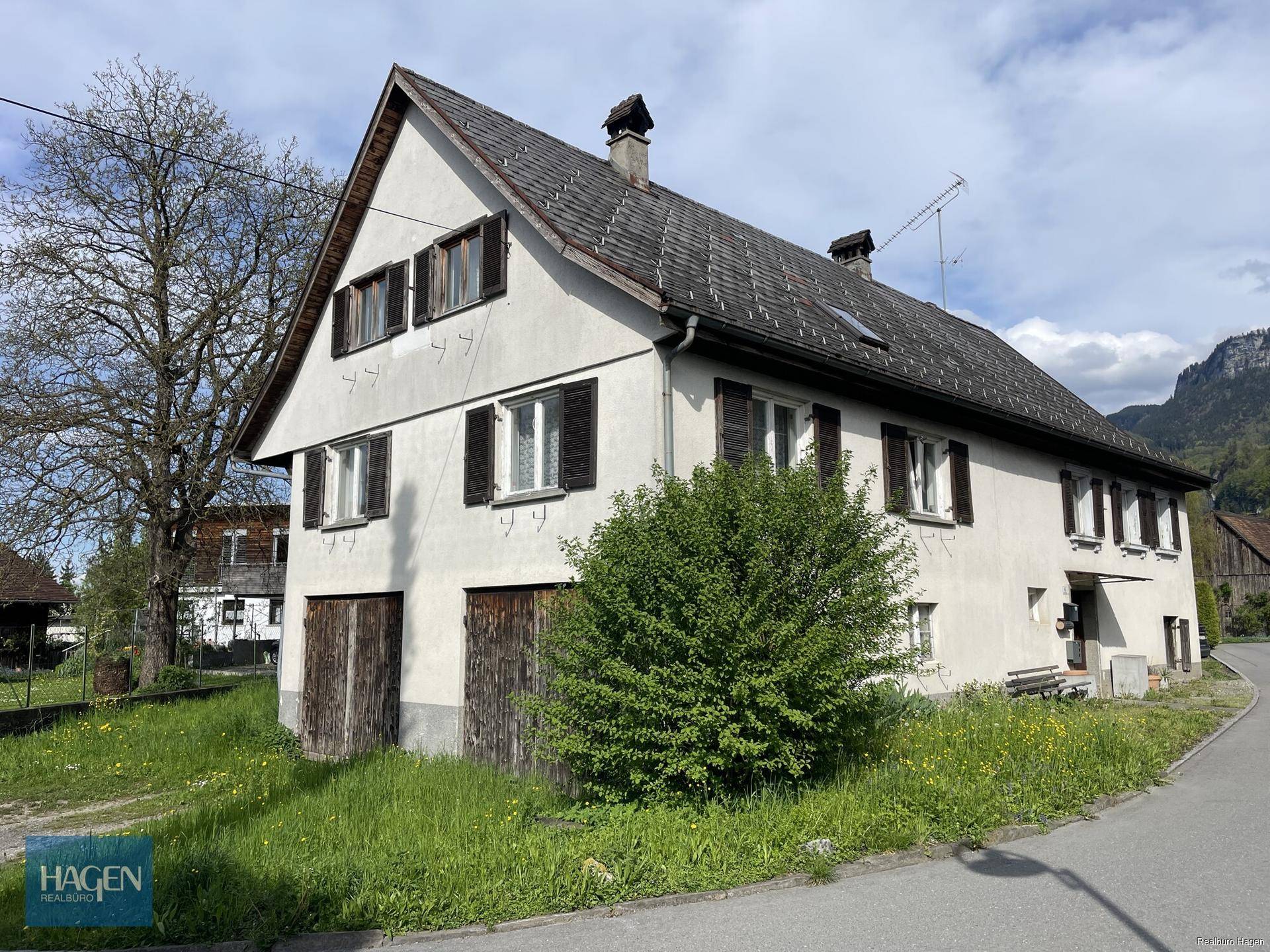 Charmantes Landhaus mit traditioneller Architektur, grüner Umgebung und Bergblick im Hintergrund.