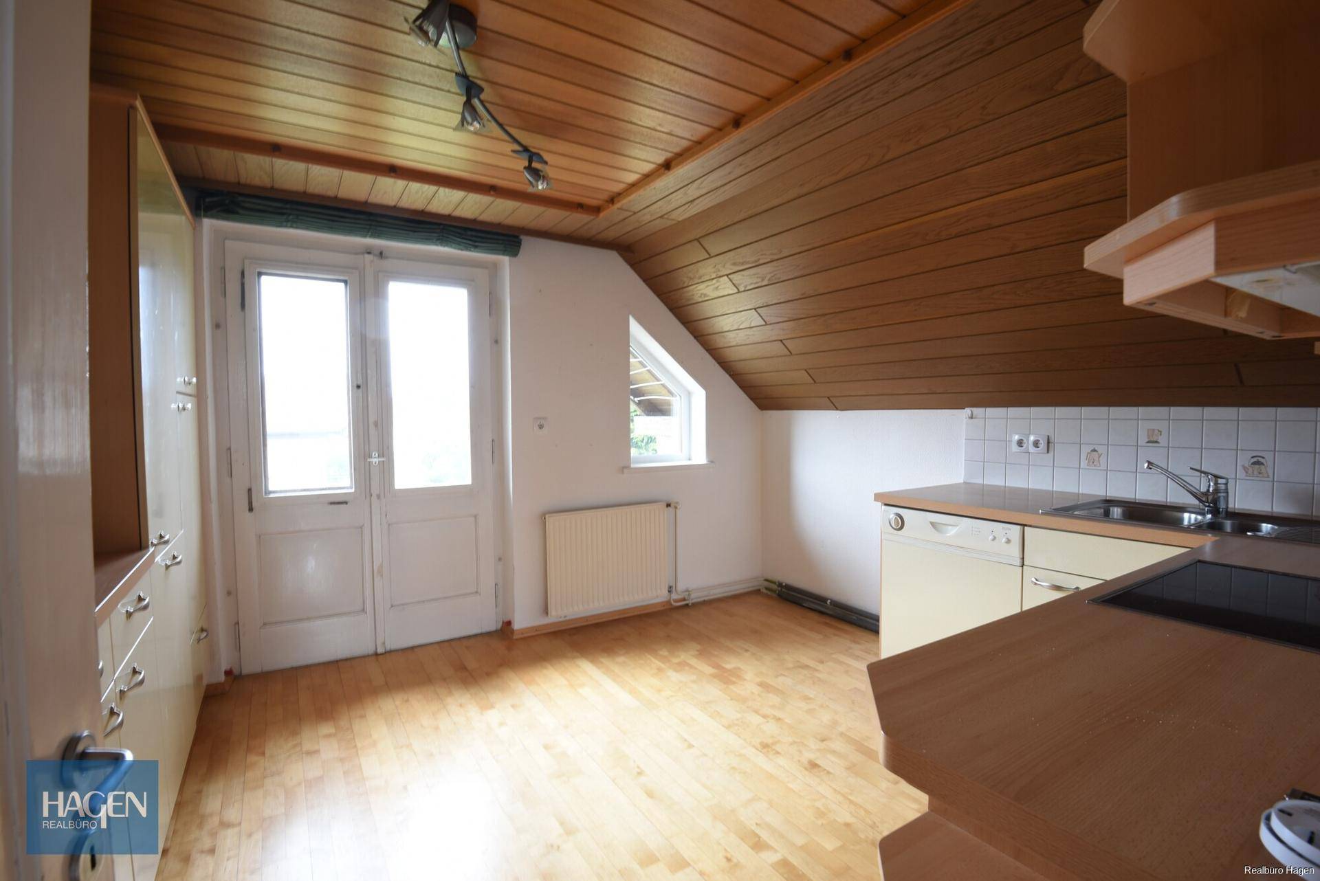 Dachgeschossküche mit schrägen Wänden, Holzboden und Zugang zu einem kleinen Balkon.