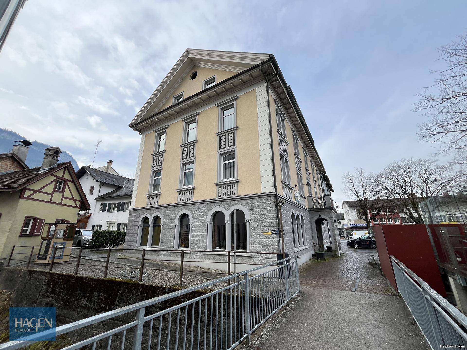 Historisches Gebäude mit gelber Fassade, grauen Arkaden und traditioneller Architektur in städtischer Umgebung.