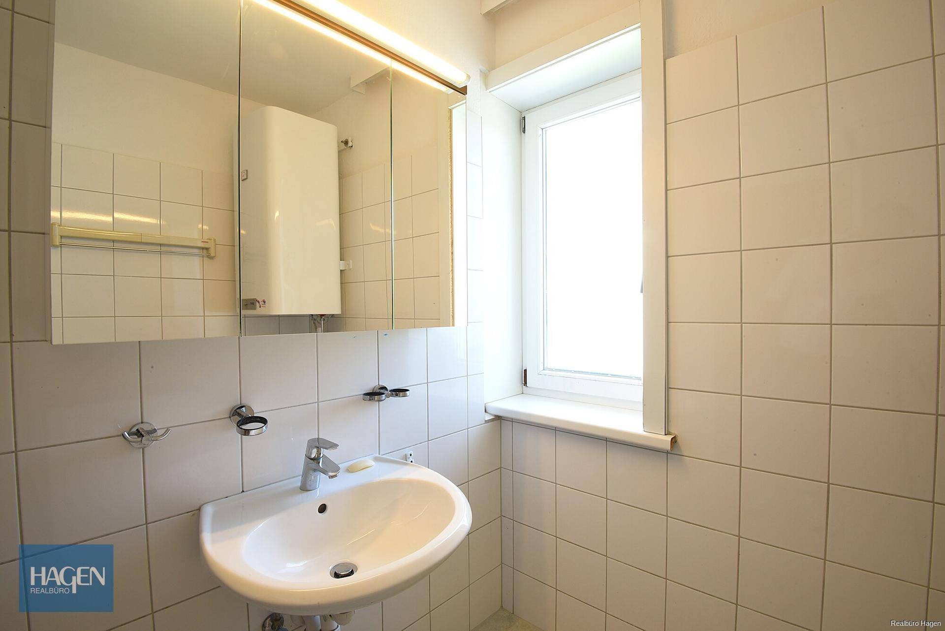 Helles Badezimmer mit Waschbecken, Spiegelschrank und Fenster für natürliche Belüftung und Tageslicht.