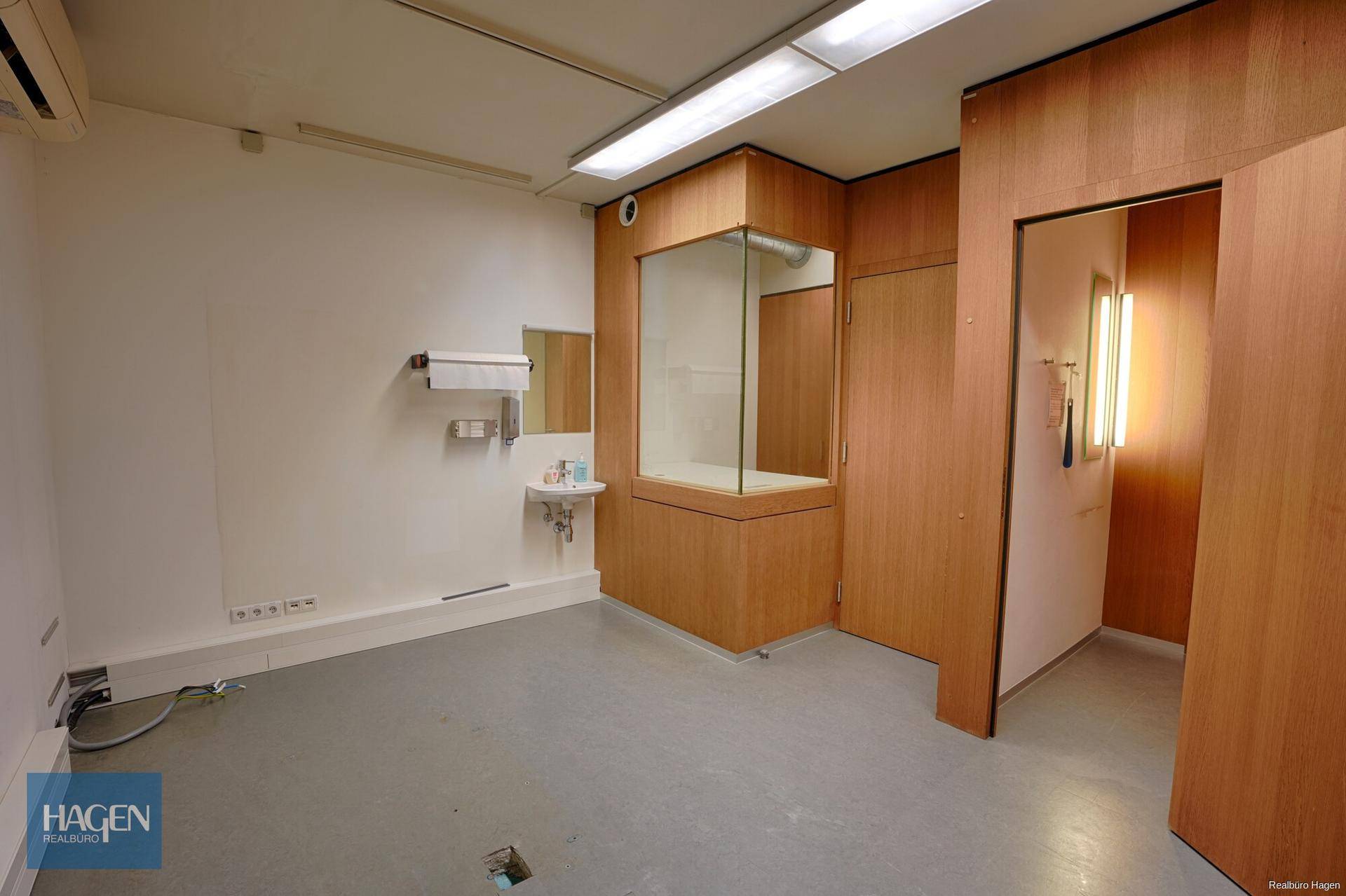 Leerer Raum mit Waschbecken, Holzverkleidung und einem Glaskasten in der Mitte.