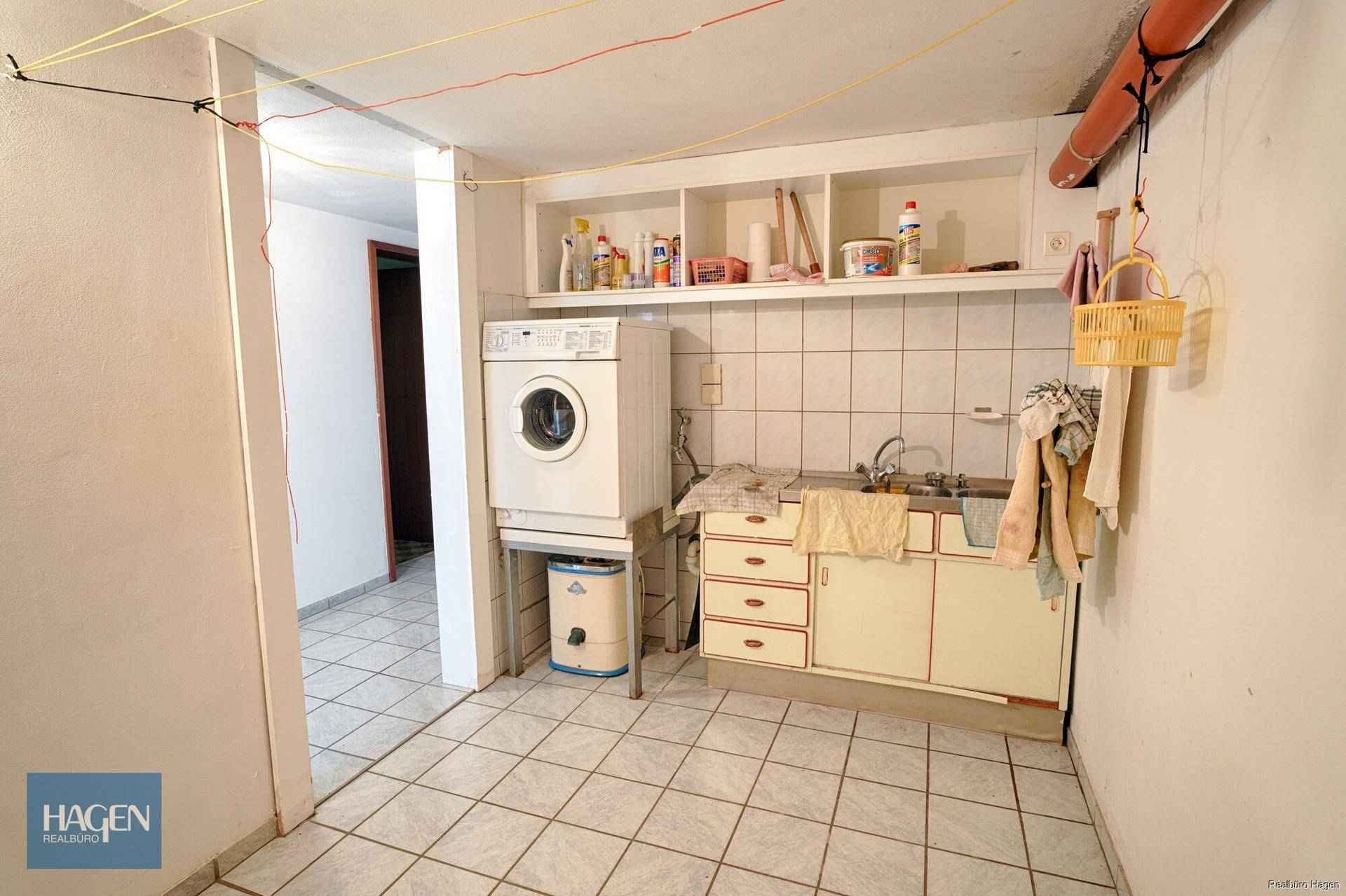 Waschküche im Keller mit Waschmaschine, Spülbecken und Fliesenboden.