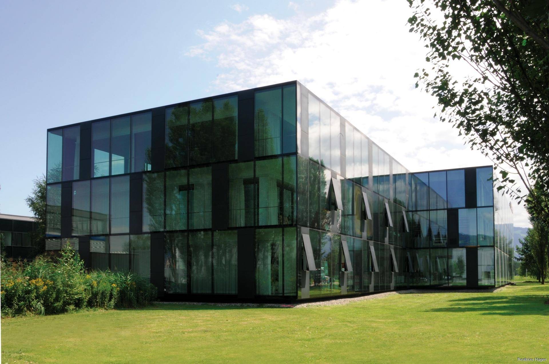 Modernes Bürogebäude mit beeindruckender Glasfassade und gepflegter Grünfläche unter blauem Himmel.