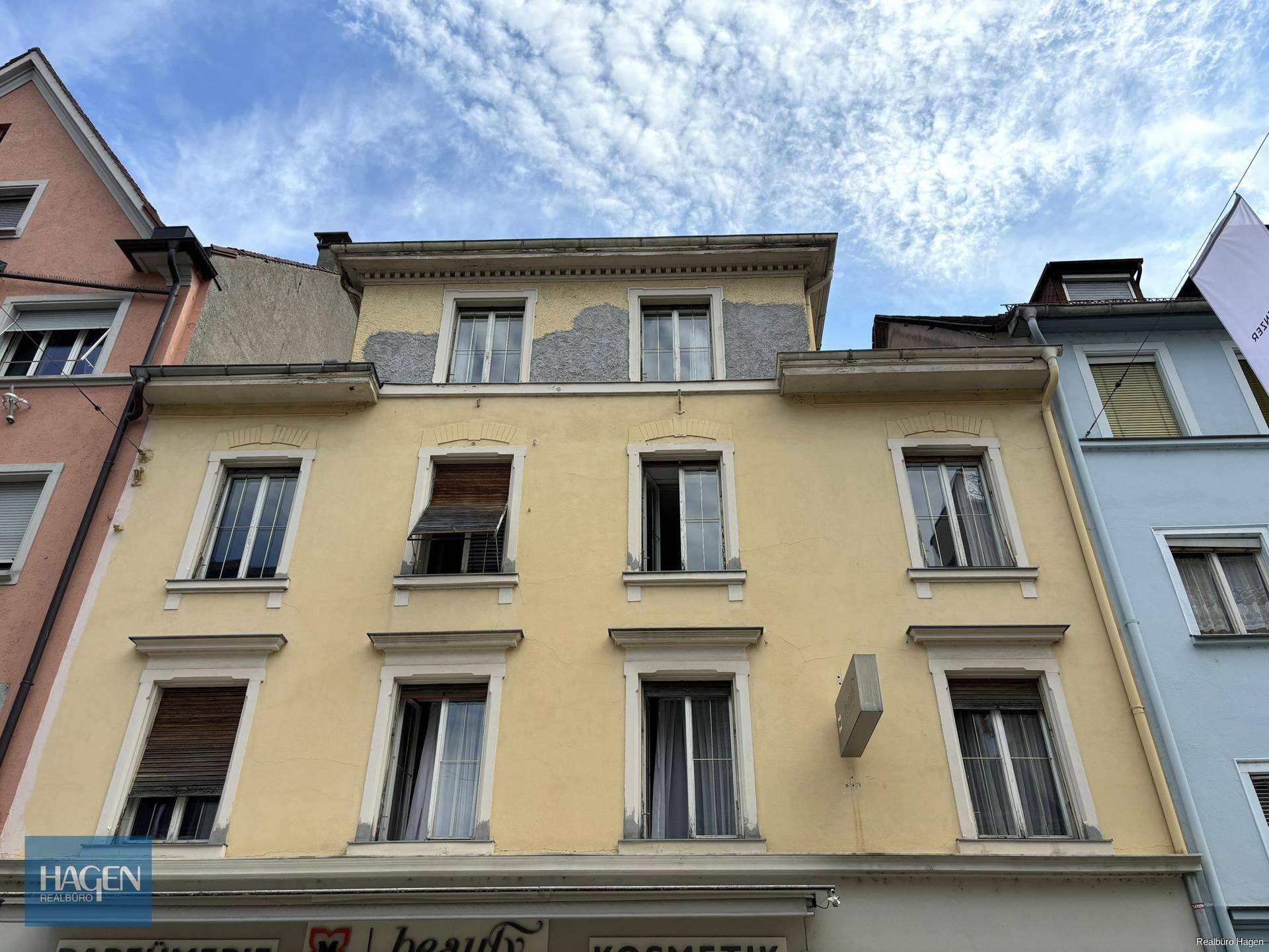 Nahaufnahme der gelben Fassade eines Altbaus mit Fenstern und sichtbaren Abnutzungsspuren.