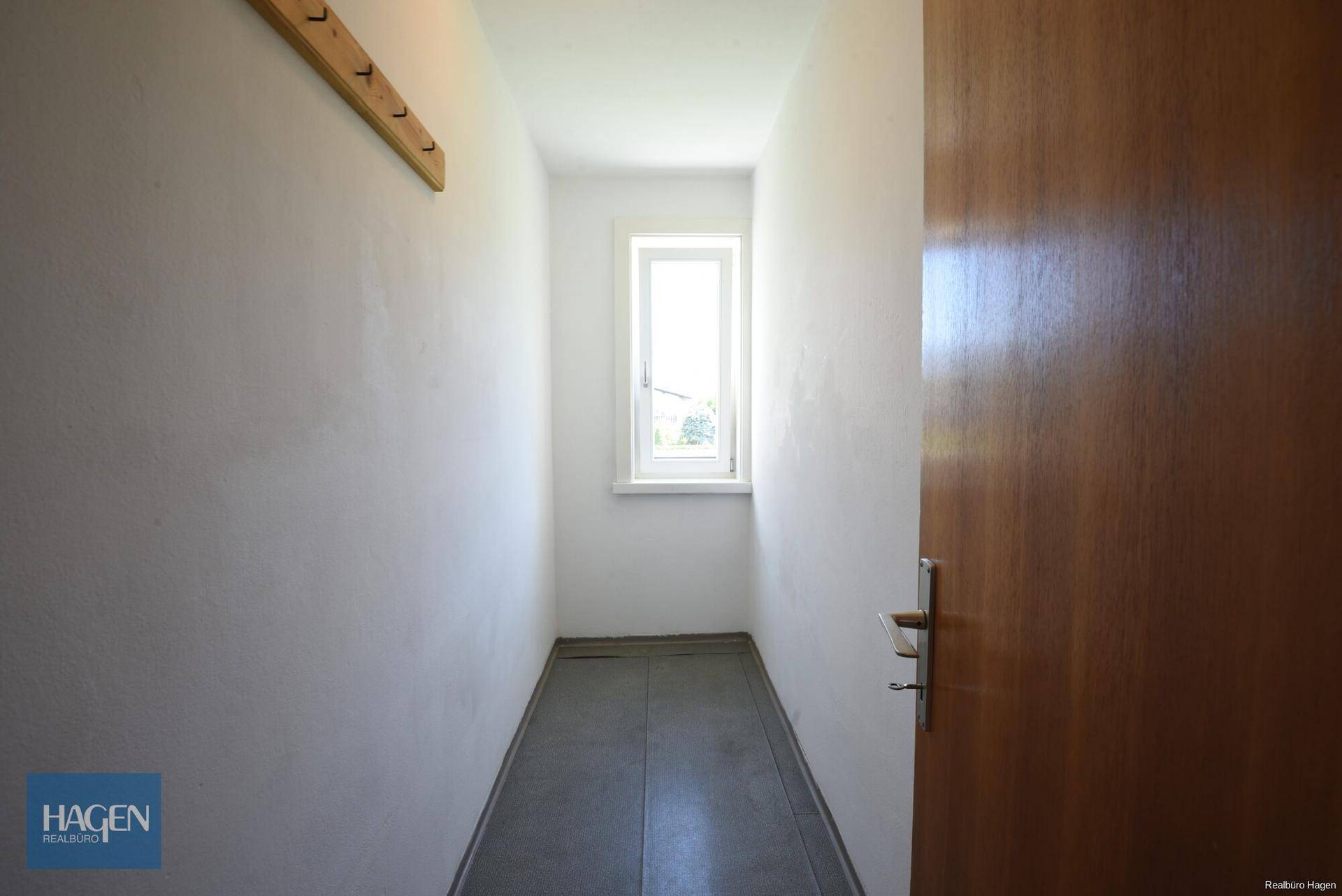 Schmaler Flur mit Fliesenboden und einem kleinen Fenster für natürliche Belüftung.