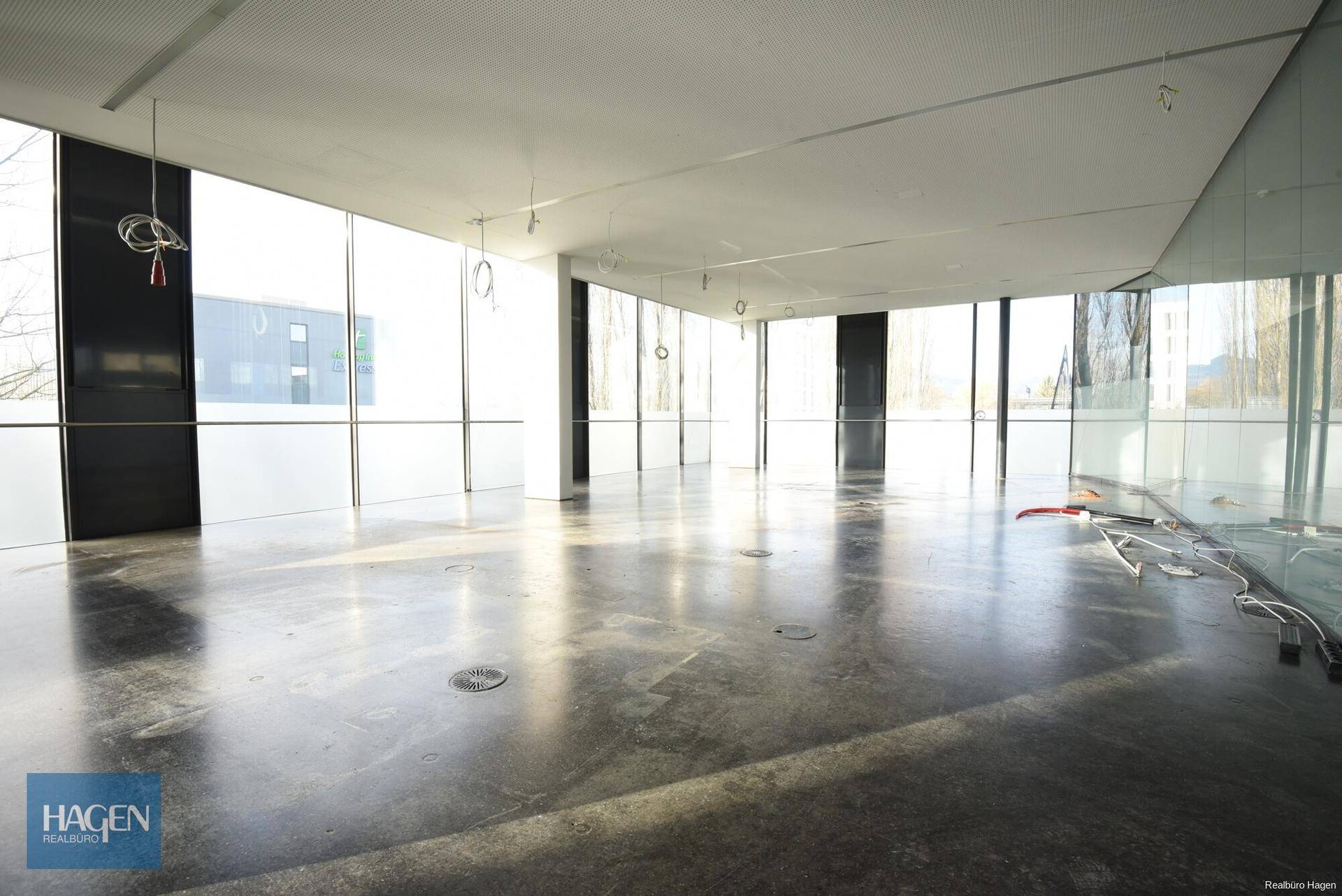 Großer, offener Bürobereich mit weitem Blick durch raumhohe Fenster und glänzendem Betonboden.