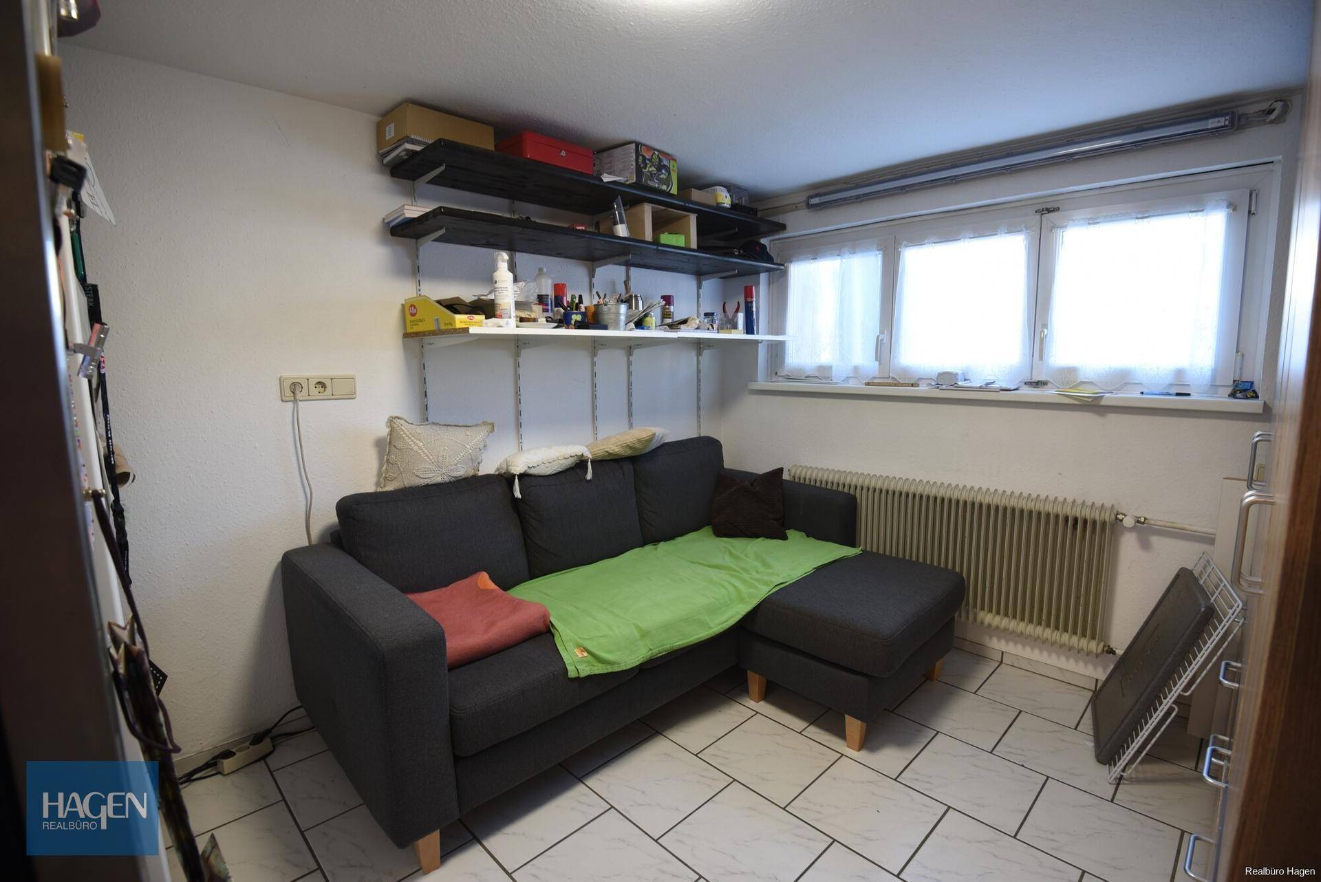 Ausgebauter Kellerraum mit Sofa, Regalen und Fenster.
