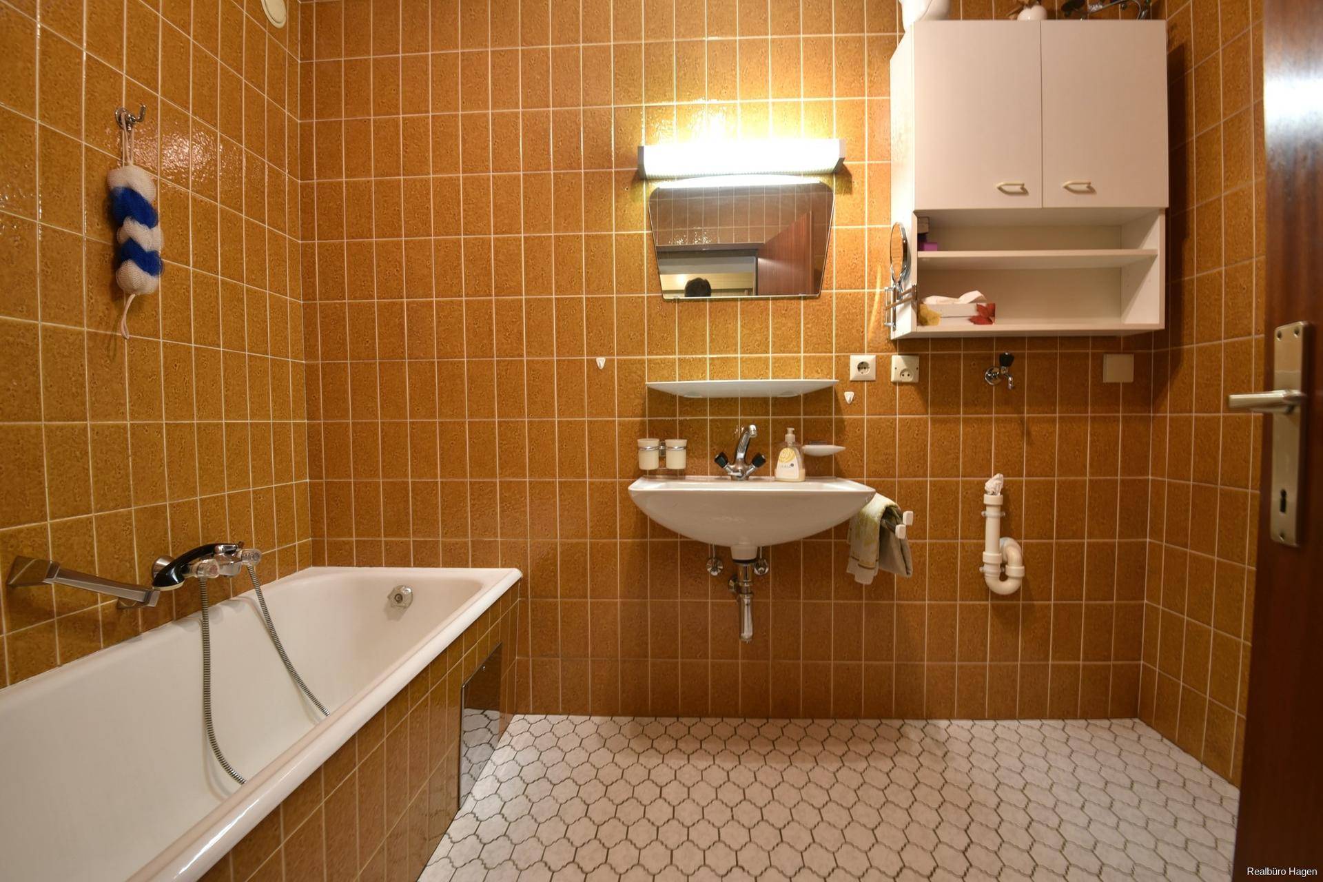 Badezimmer mit orangefarbenen Wandfliesen, weißem Sechseck-Boden und einer Badewanne mit Einzelwaschbecken.