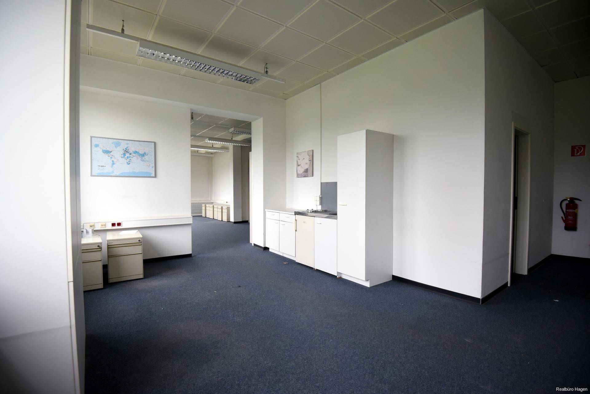 Heller Bürobereich mit kleiner Küchenzeile, Teppichboden und einer Weltkarte an der Wand.