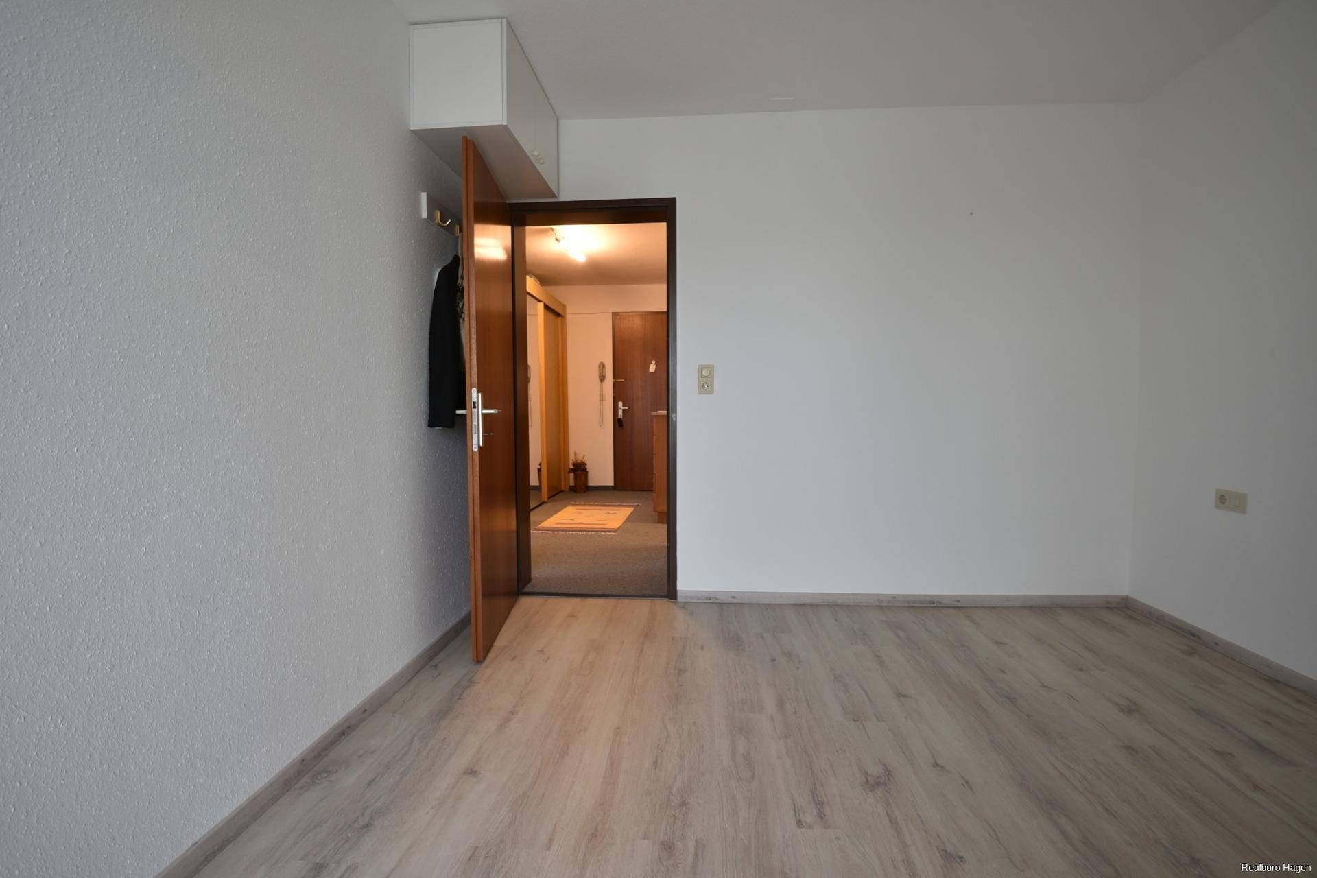 Leeres Zimmer mit Laminatboden und Garderobe am Eingang, mit Blick in den Flur.