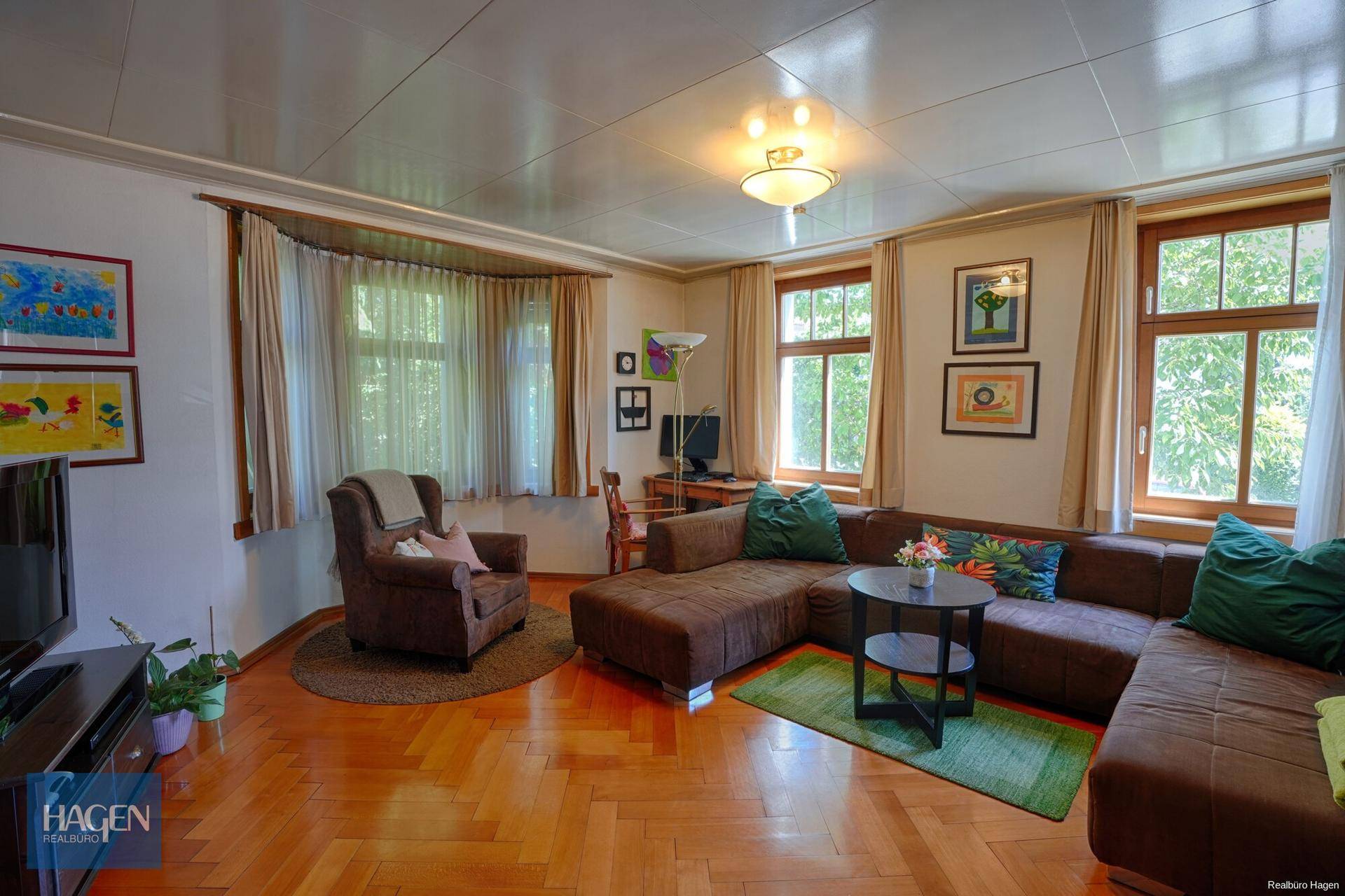 Gemütliches Wohnzimmer mit Fischgrätparkett, großem Ecksofa und hellem Erkerfenster.