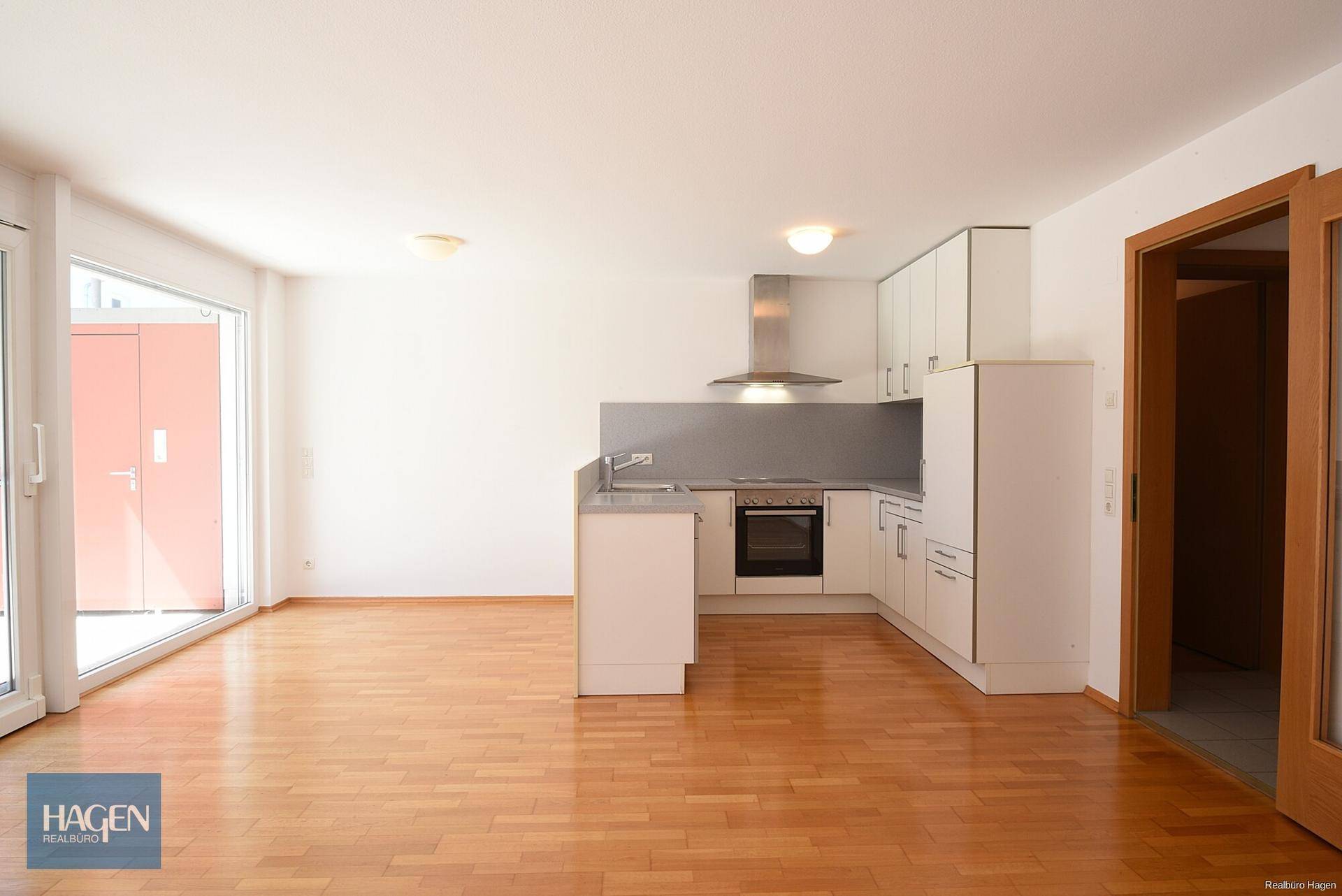 Offener Wohnbereich mit integrierter Küche, Parkettboden und Zugang zur Terrasse.