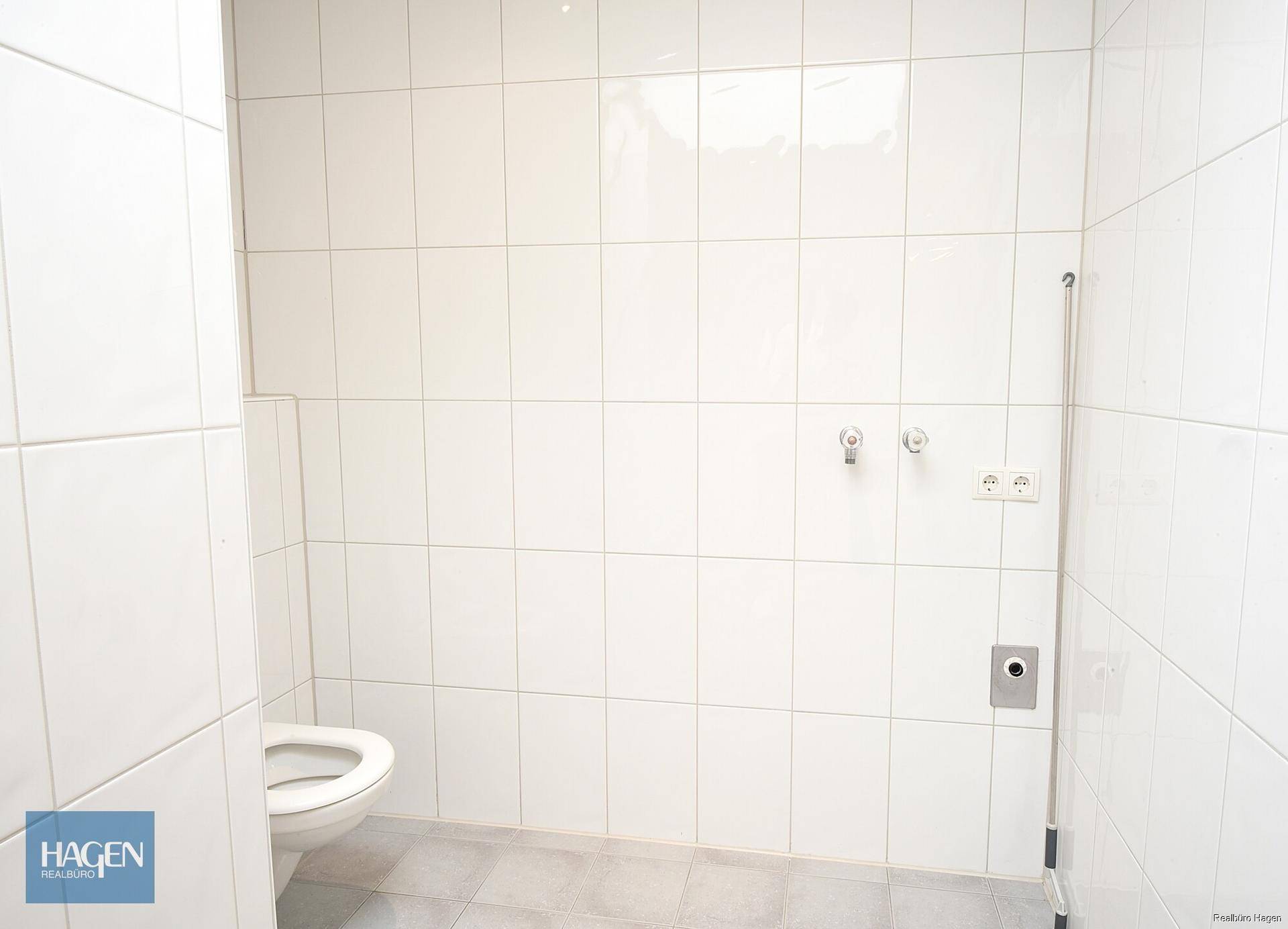 Sauber gefliestes Badezimmer mit Toilette und Anschlüssen für eine Waschmaschine.