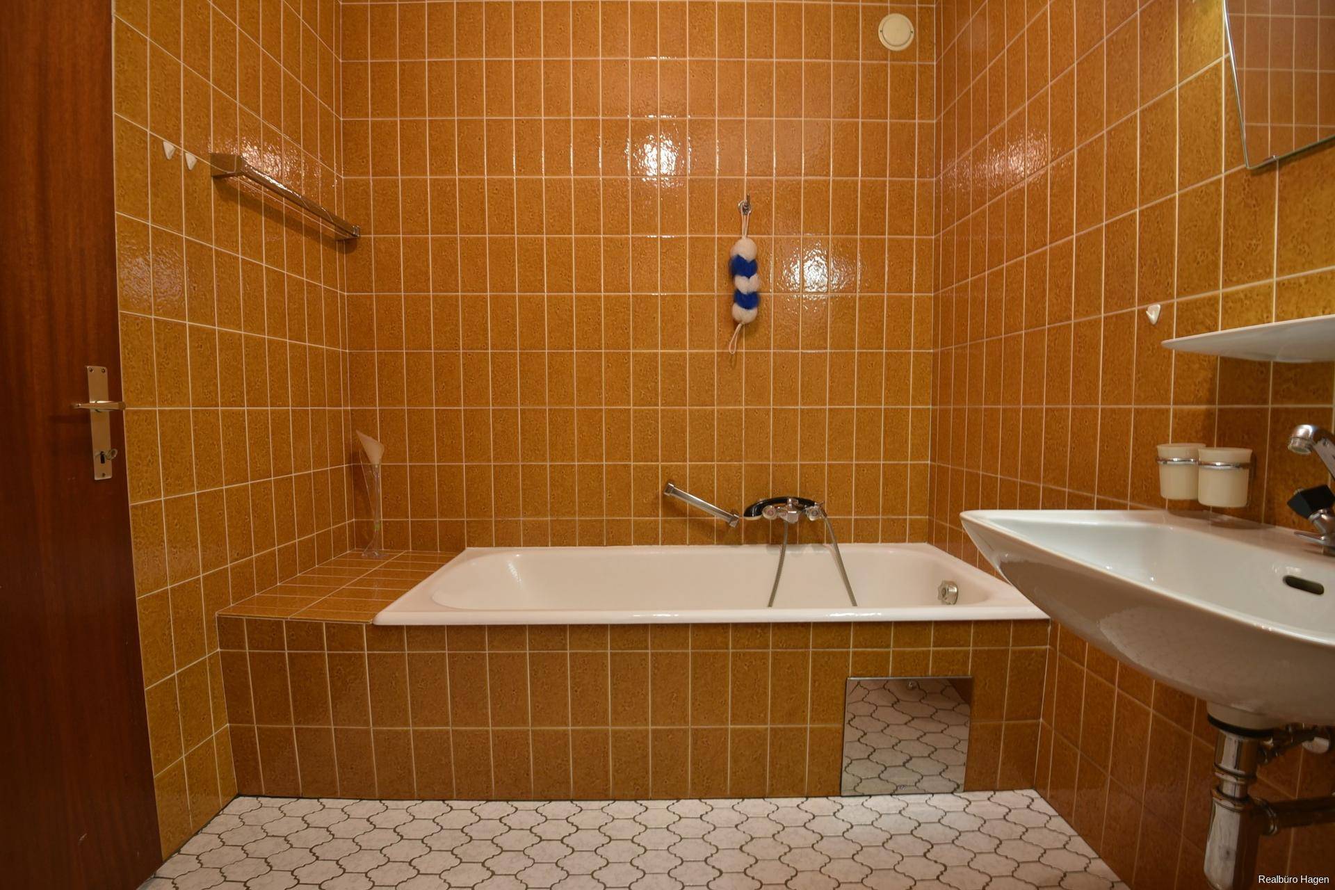 Detailansicht des Badezimmers mit orangefarbenen Fliesen, Badewanne und Waschbecken.