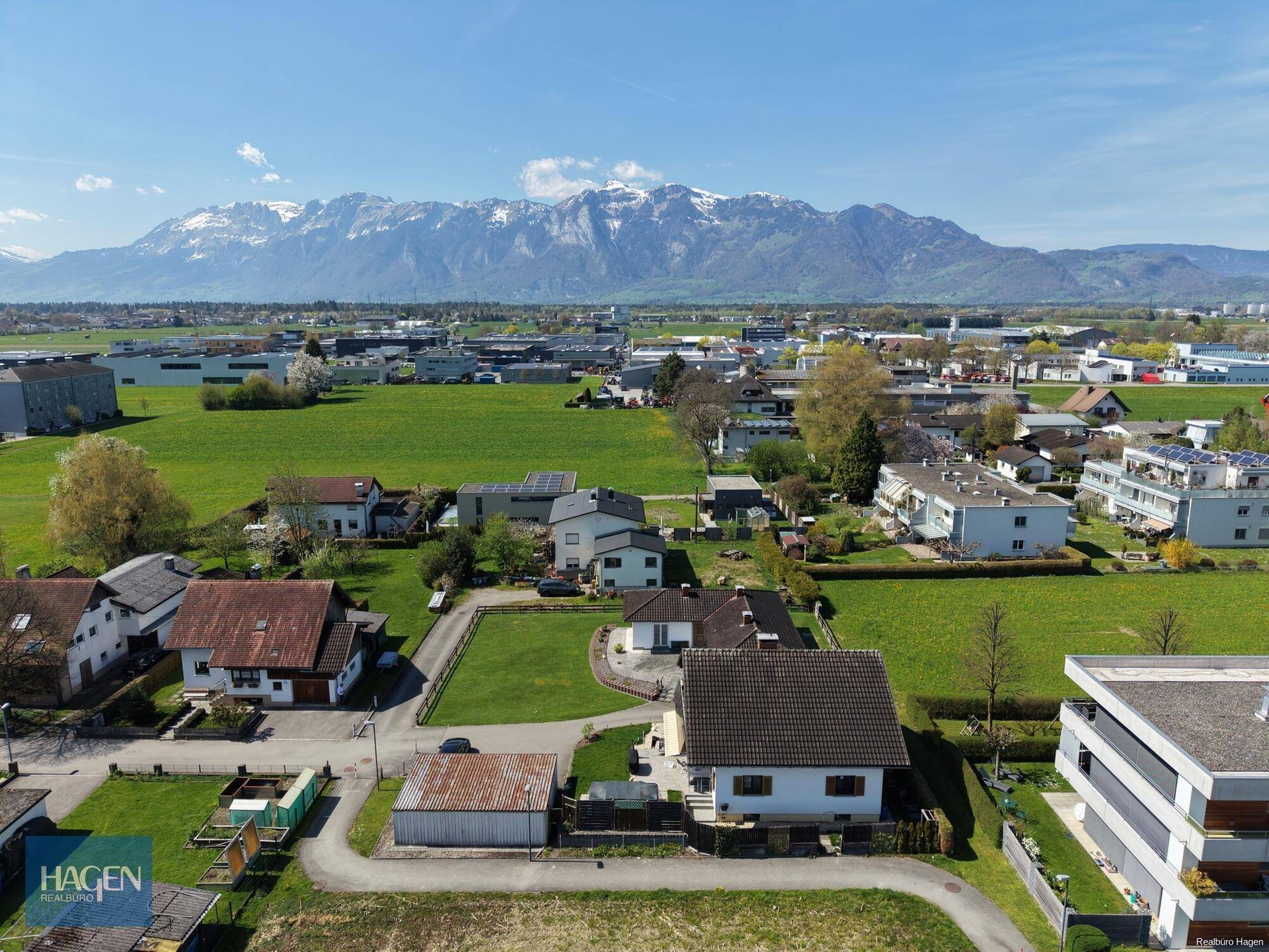 Panoramablick über die ländliche Umgebung mit Wohngebäuden und einer beeindruckenden Bergkette.
