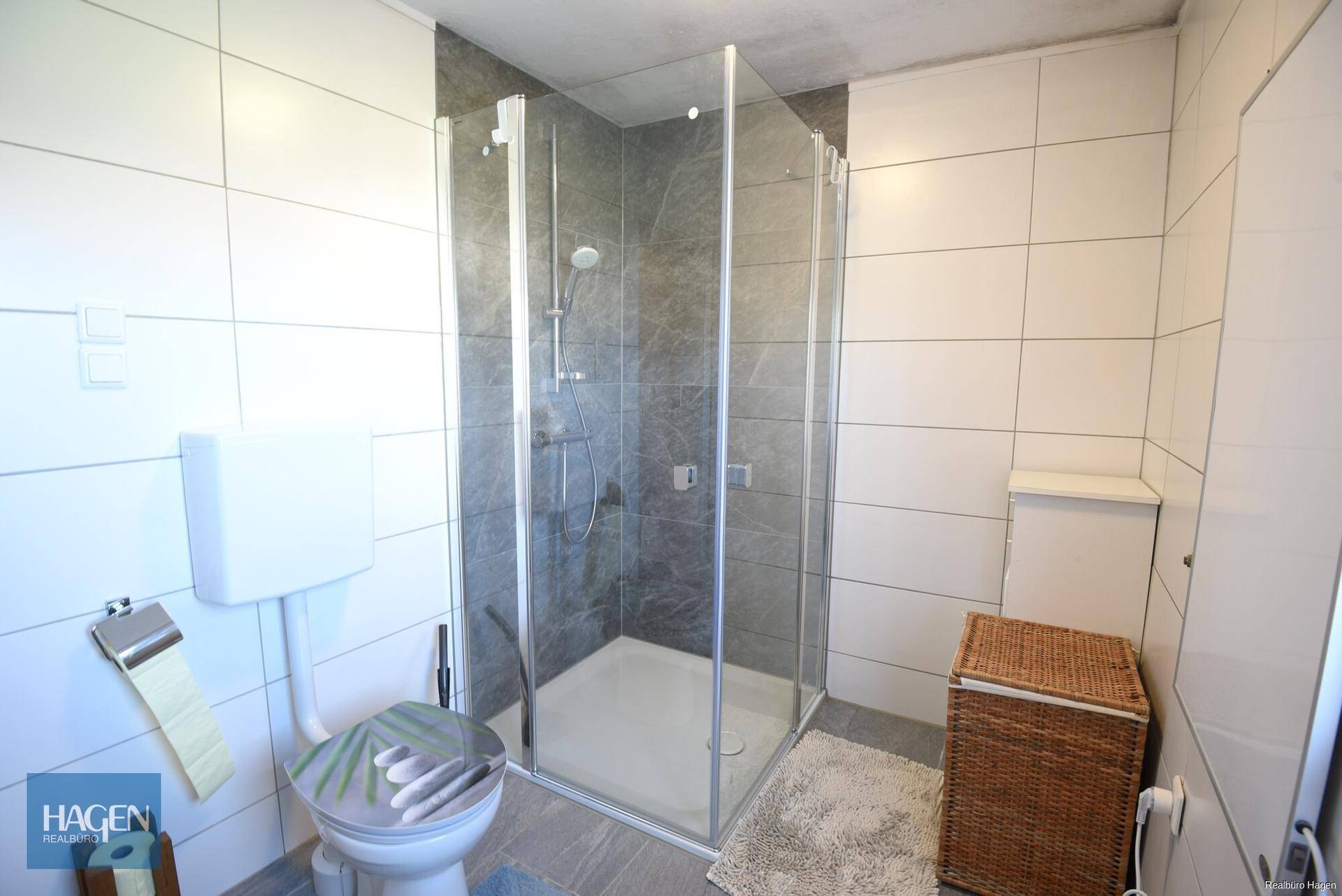 Badezimmer mit Duschkabine, WC und hellen Wand- und Bodenfliesen.
