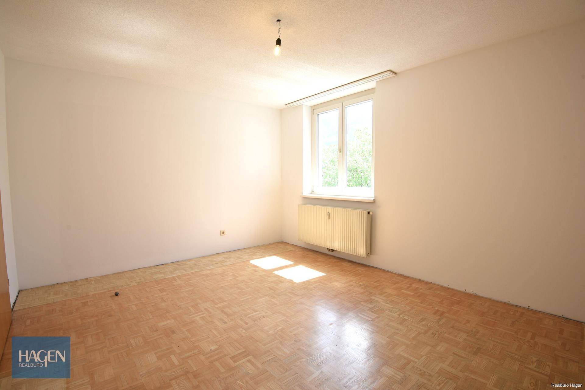 Lichtdurchfluteter Raum mit Parkettboden und Heizkörper unter dem Fenster.