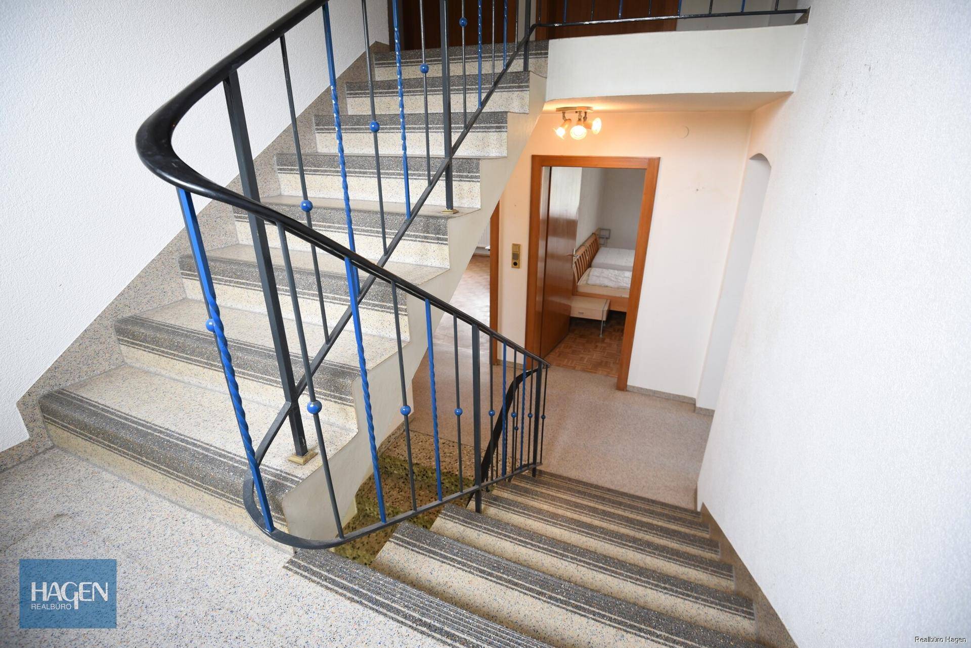 Treppenhaus mit Terrazzoboden und schmiedeeisernem Geländer, das zu den oberen Etagen führt.