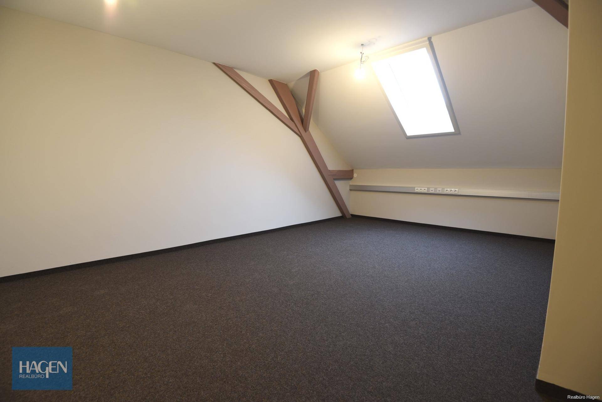Geräumiger Dachbodenraum mit sichtbaren Holzbalken, Dachschräge und einem hellen Dachfenster.