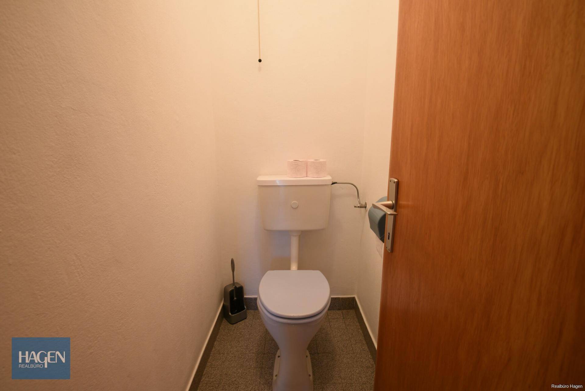 Separate Toilette mit WC und Fliesenboden in neutralen Farben.
