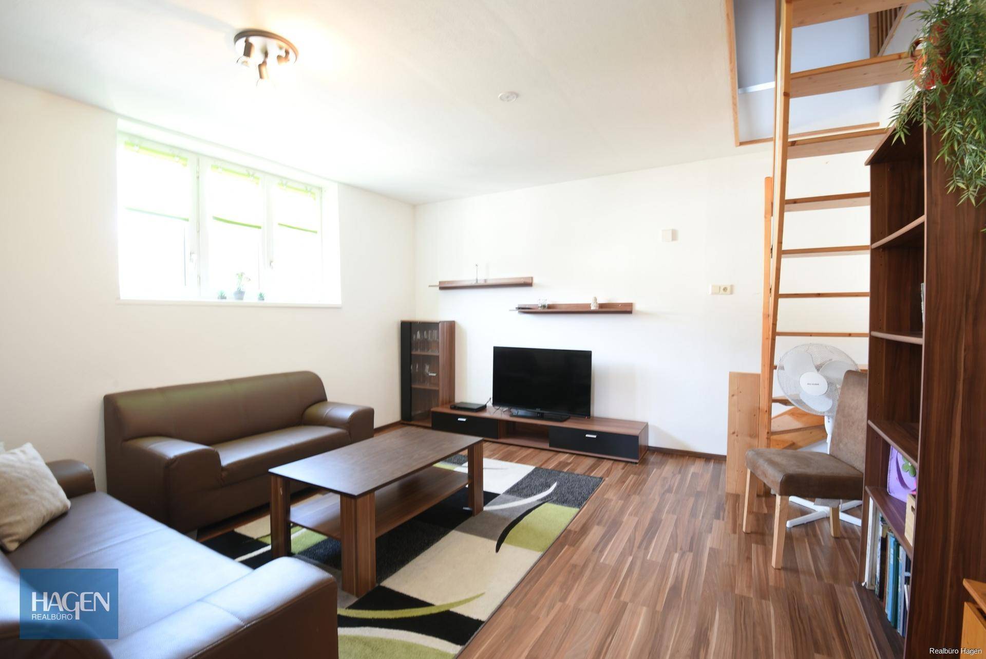 Geräumiges Wohnzimmer mit bequemen Sofas, Fernseher und einer Holztreppe zu einer oberen Ebene.