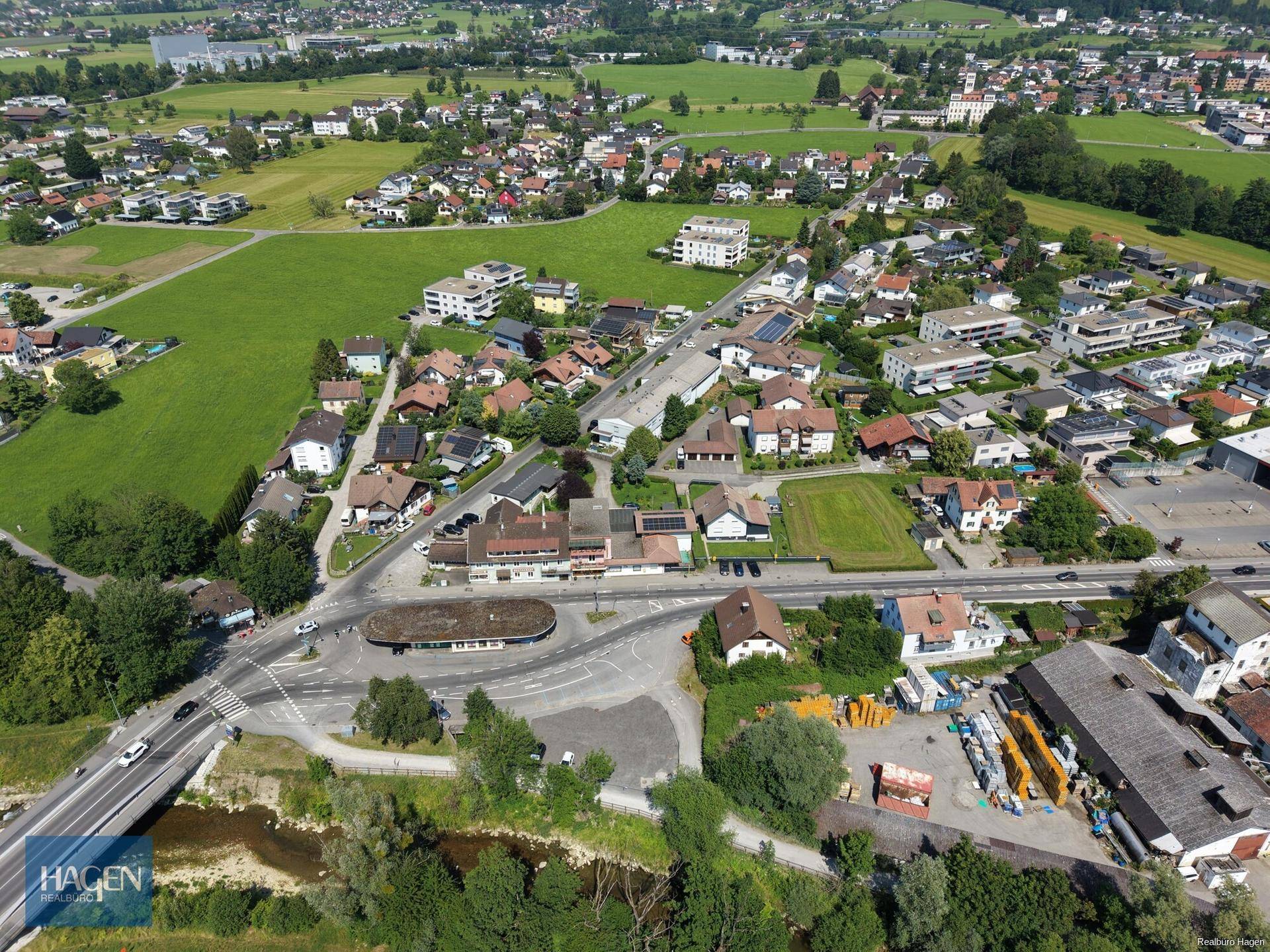 Luftaufnahme einer Stadt mit angrenzender Landschaft, Feldern und einem Fluss unter klarem Himmel.