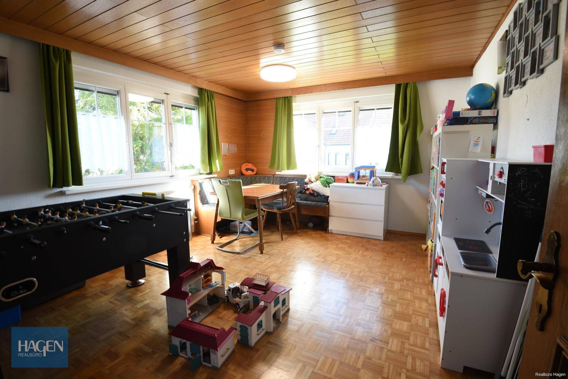 Helles Zimmer mit Holzdecke, Parkettboden und Spielbereich für Kinder.