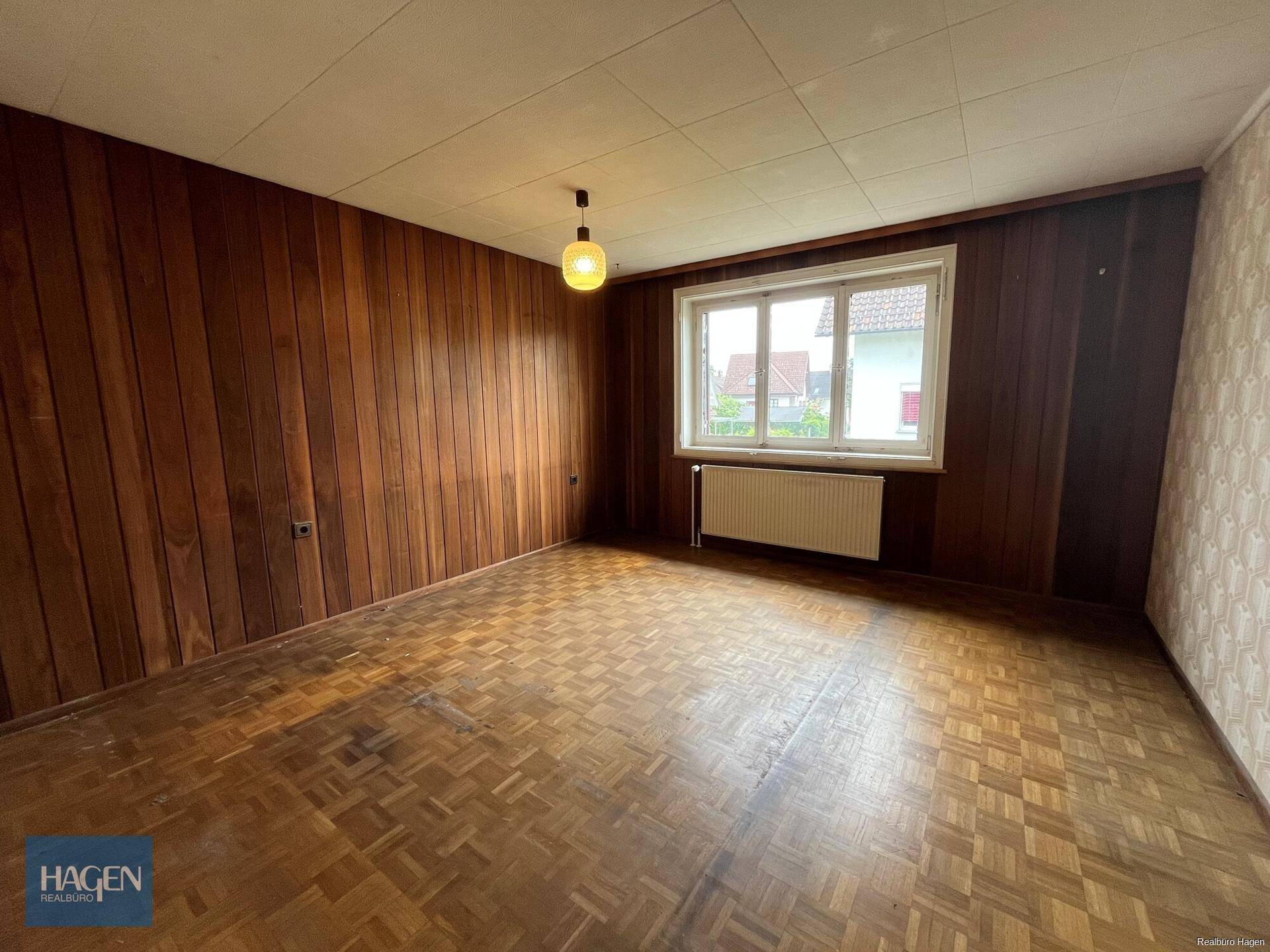 Schlafzimmer mit Holzvertäfelung, Parkettboden und Fenster mit Blick ins Grüne.
